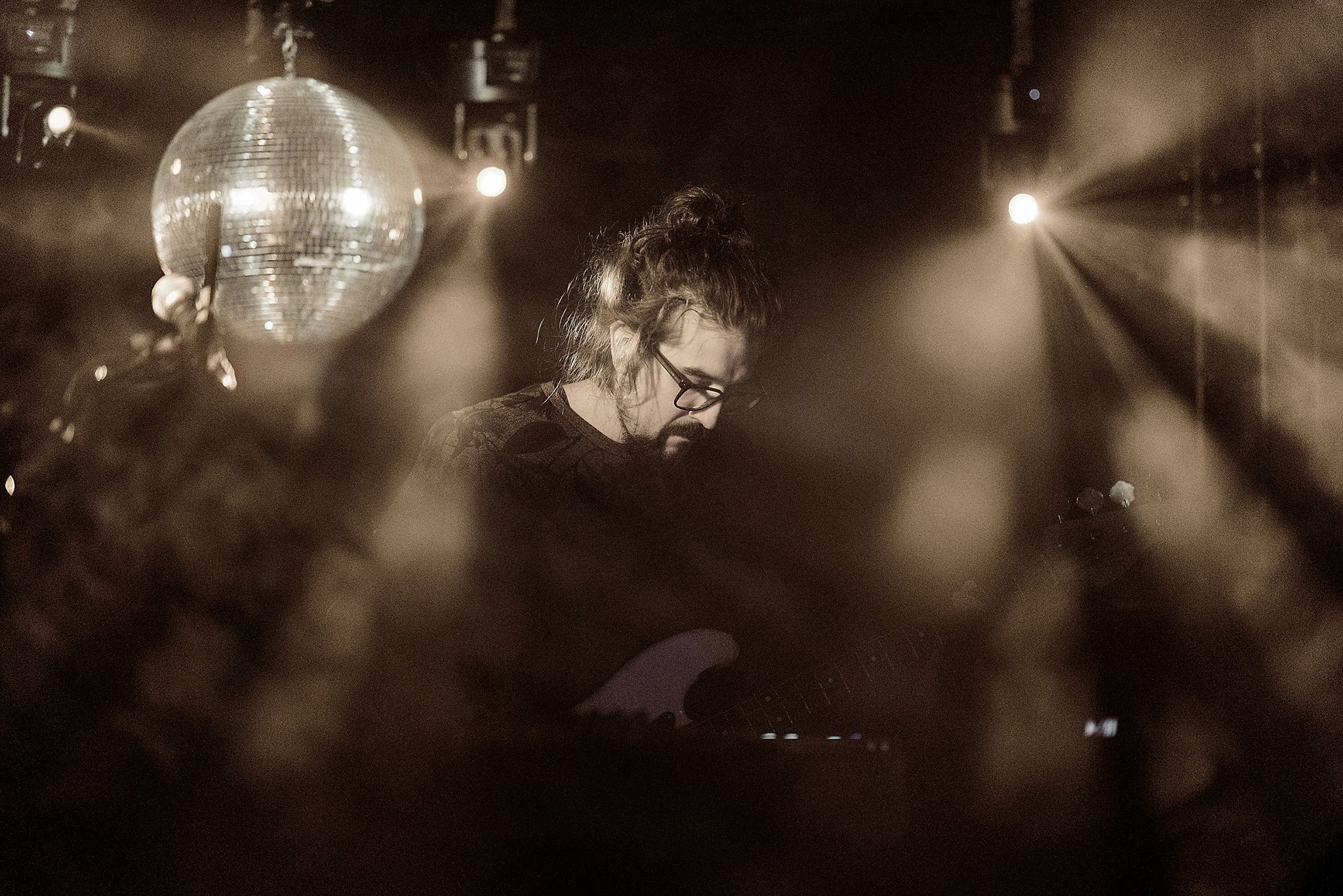 Film clapperboard in focus with glowing orange background, misty street, and silhouettes of people and lights; conveys mystery and anticipation.