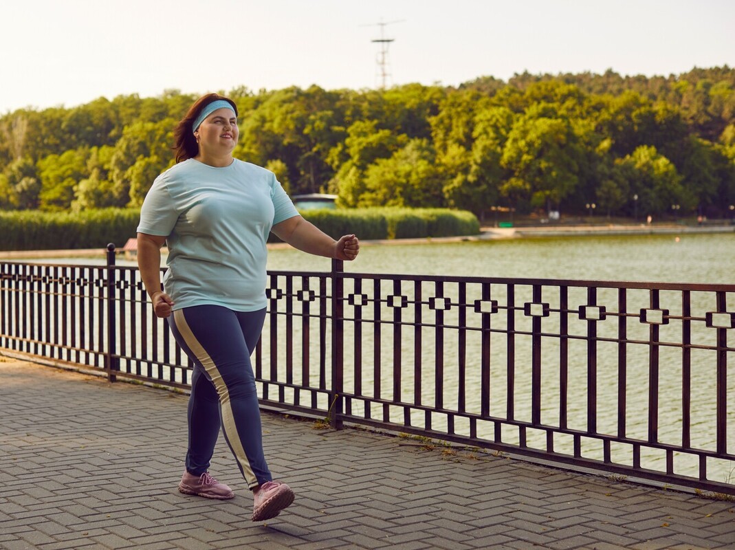 overweight woman smiling as she successfully reaches how many miles of walking to lose weight she needs to do on a path by a lake
