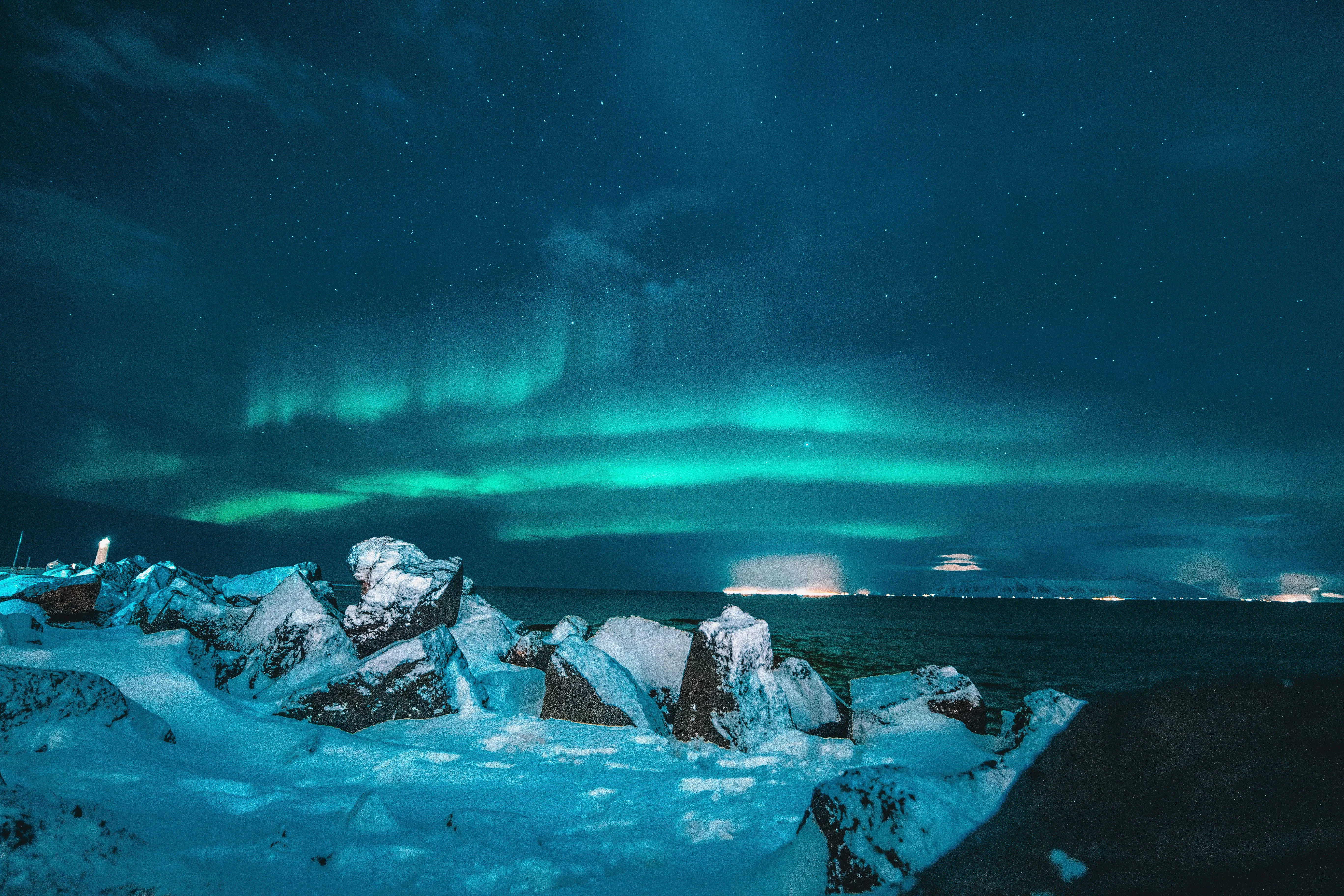 Bright green Northern Lights shining over a frozen lagoon filled with blue icebergs and snow.
