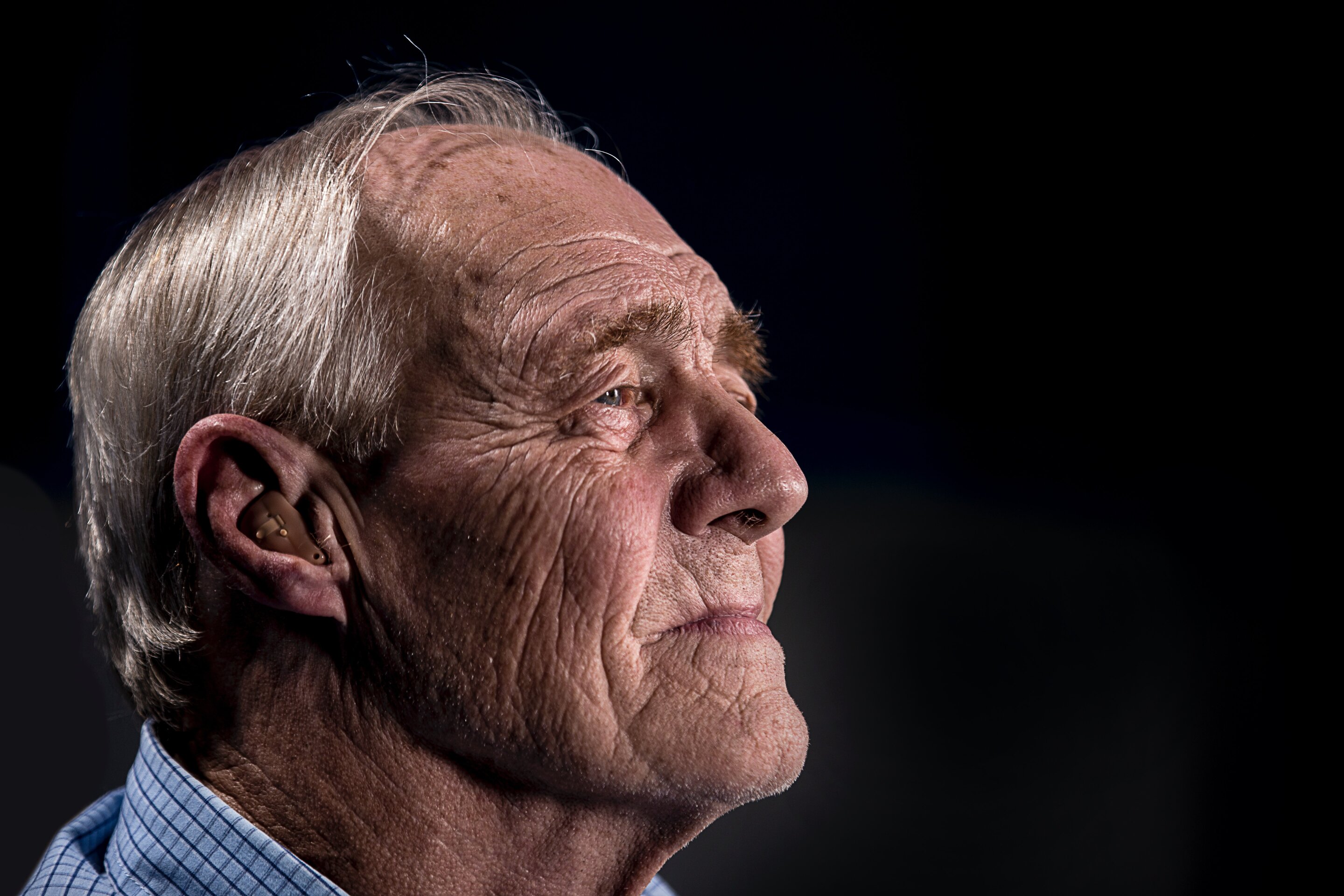 Close-up of an older man with silver hair and a thoughtful expression, against a dark background.