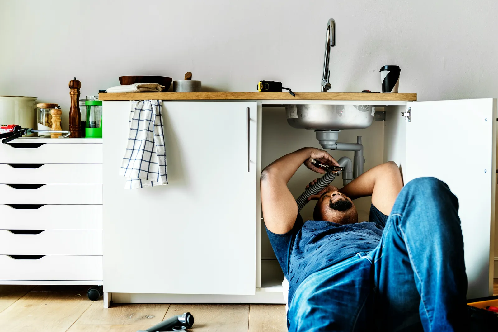 Man lying under kitchen sink cabinet repairing plumbing