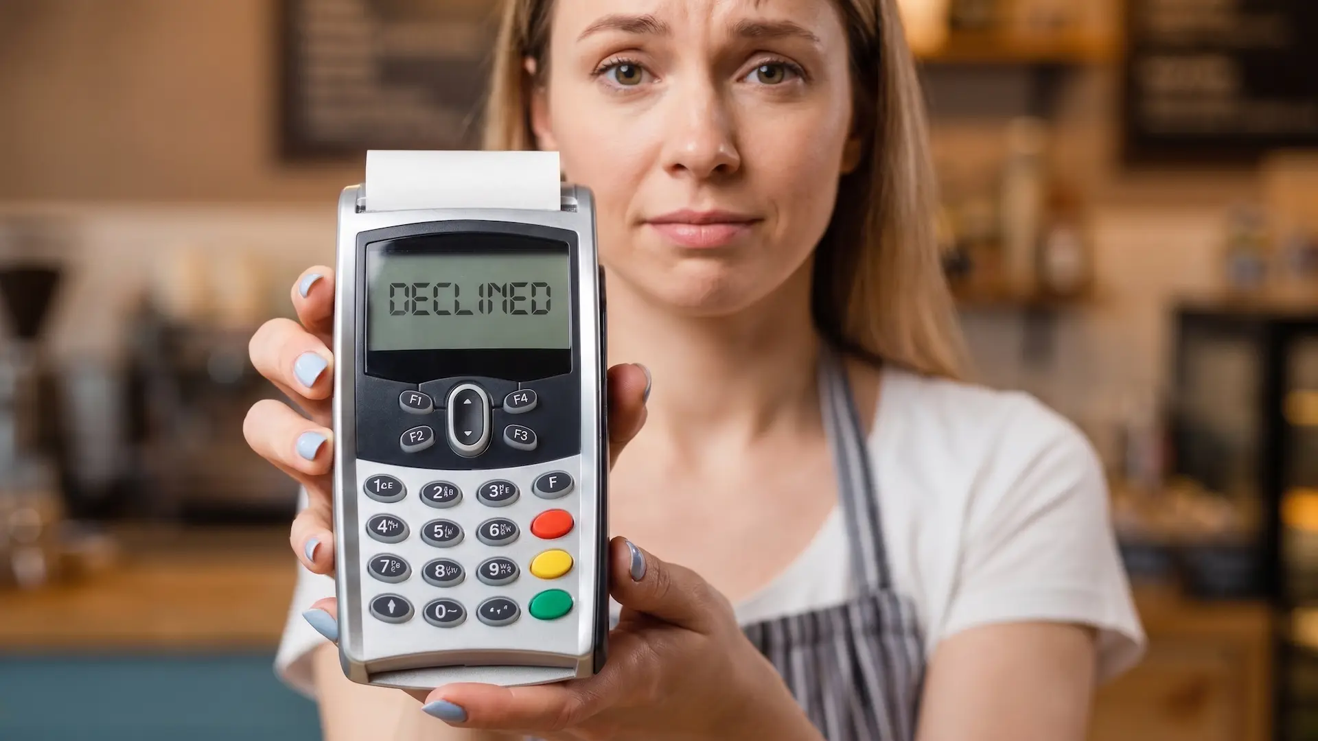 A shop worker holds out a card payment terminal; its display reads DECLINED.