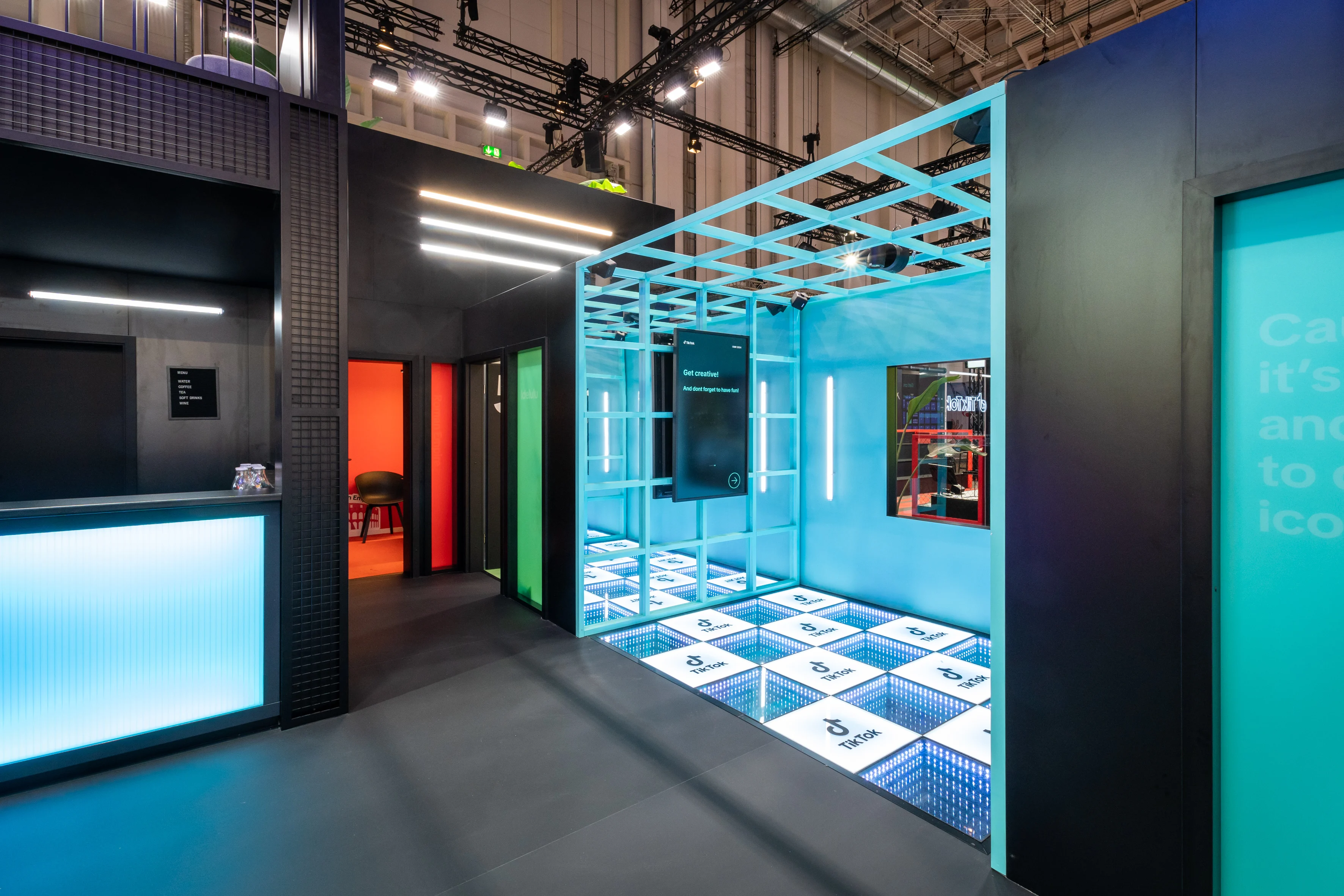 Turquoise grid cube with glowing logo floor and screen next to colorful doors inside the TikTok booth at OMR.
