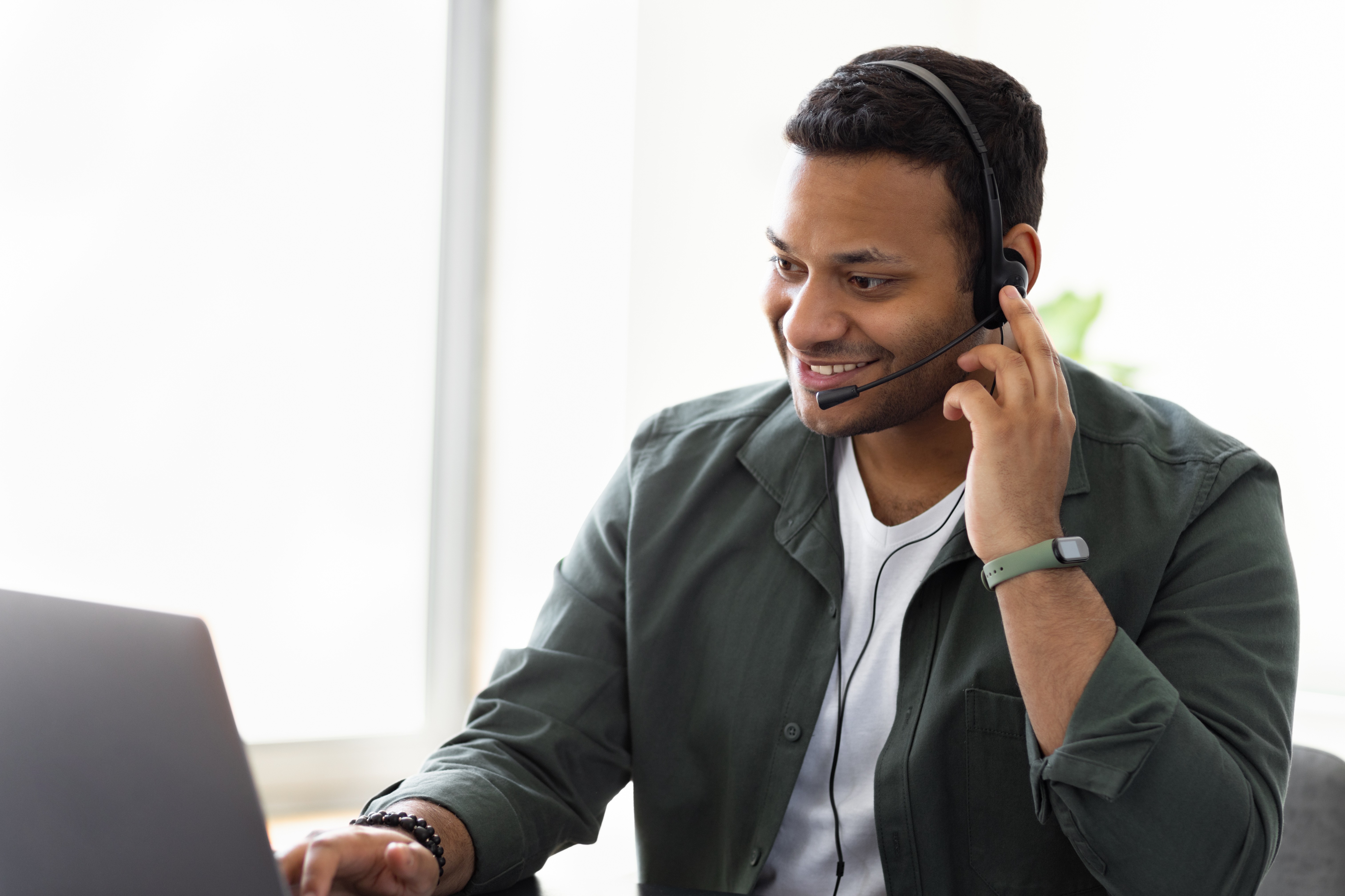 A smiling offshore employee wearing a headset, engaged in a video call on a laptop, exemplifying integration and effective communication in remote work.