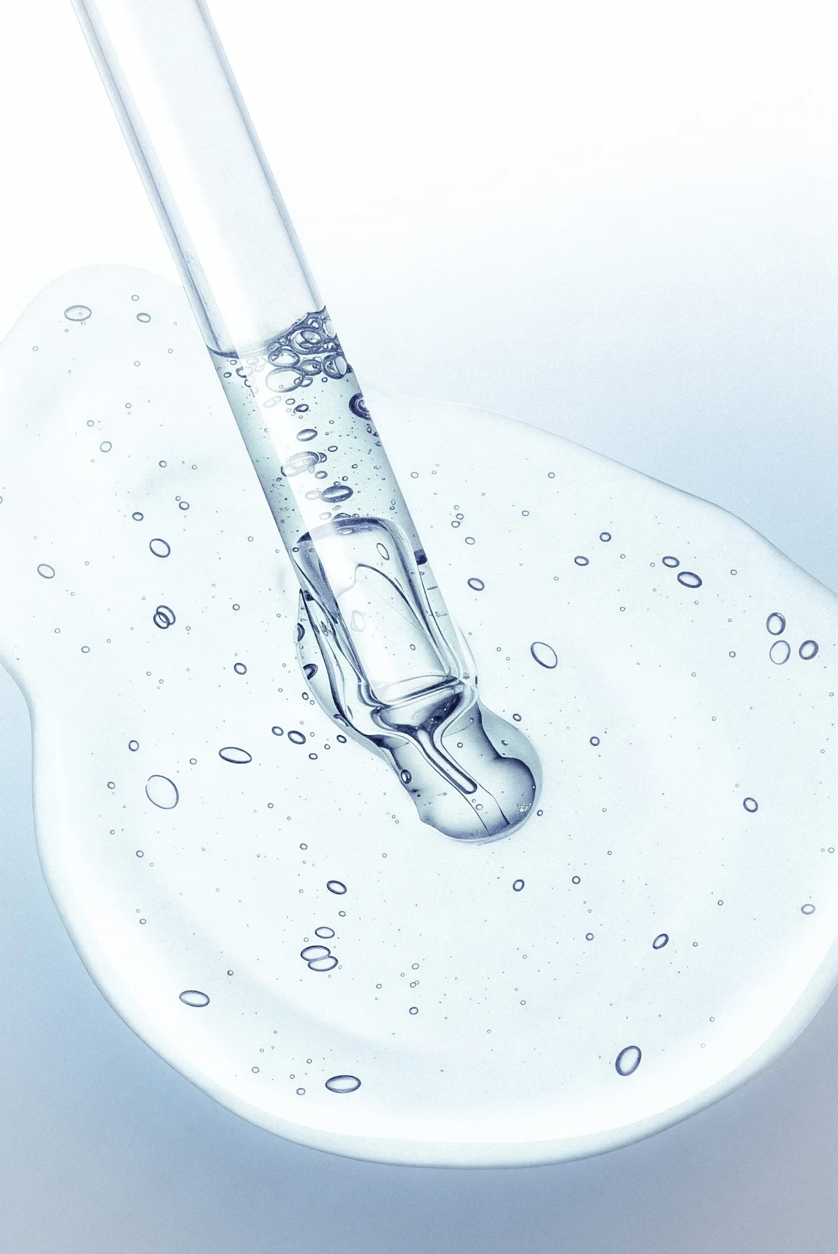 Macro photograph of a glass test tube containing vivid blue liquid with bubbles, resting on a reflective surface surrounded by laboratory glassware, representing in-vitro research and purity analysis.