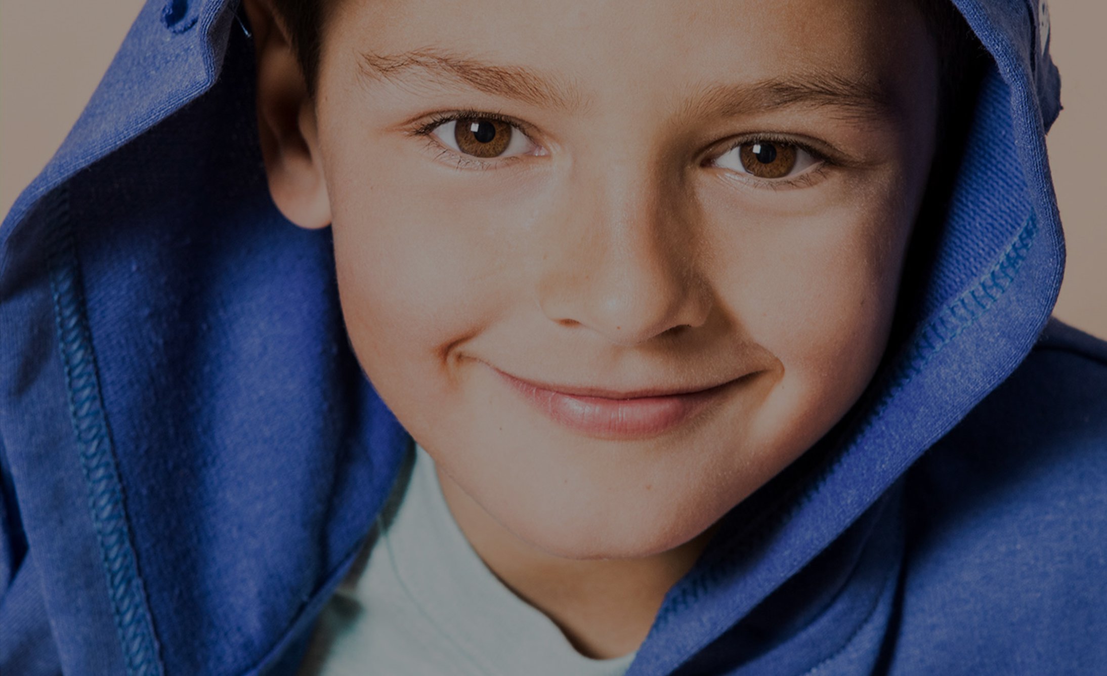 Smiling boy wearing a bright blue hoodie, focusing on his joyful expression and twinkling eyes. The hoodie adds a casual, playful tone to the image.