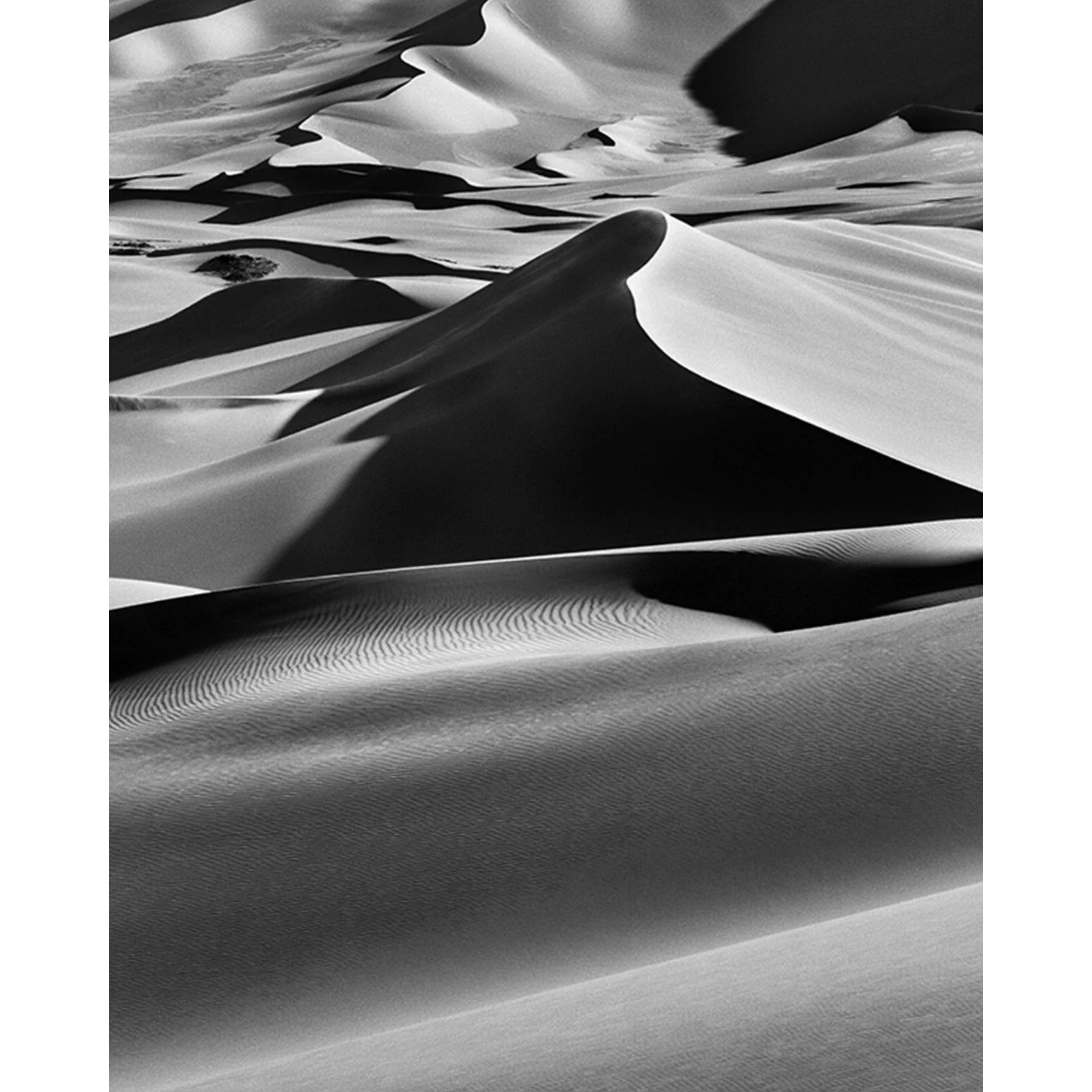 Aerial view of an expansive desert landscape of layered dunes and deep shadows converging toward a central peak, black and white