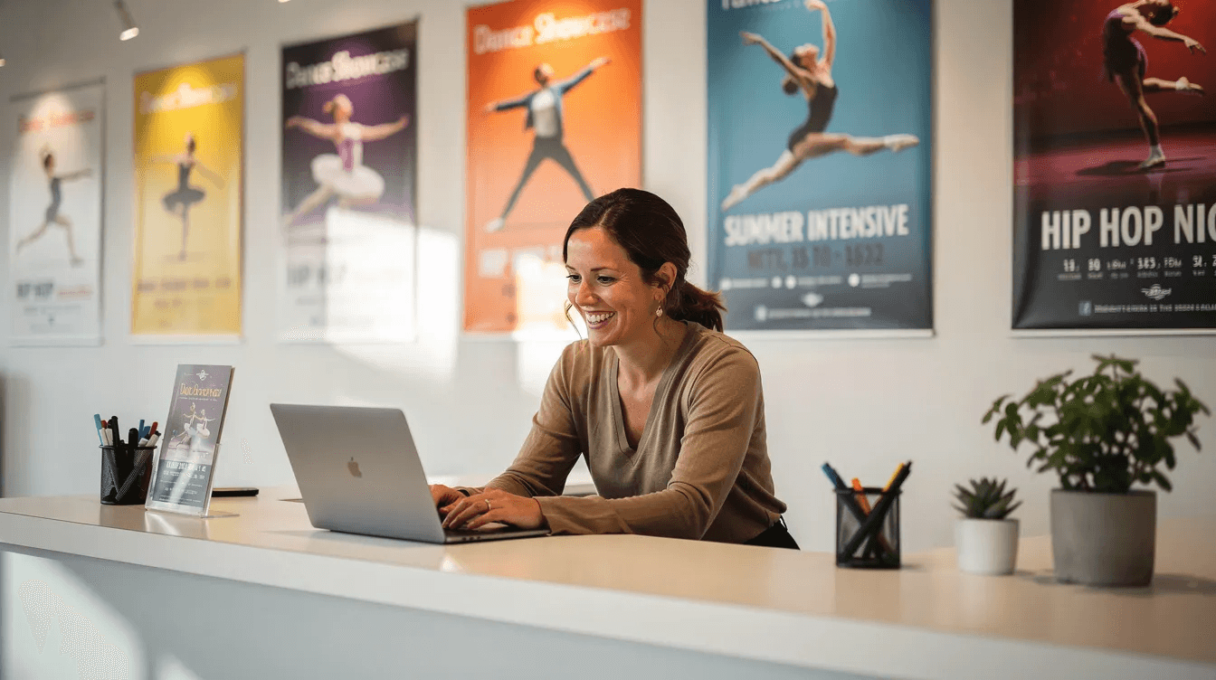 A smiling studio owner is seated at a reception desk, working on a laptop surrounded by vibrant dance posters. This image captures the essence of studio management, showcasing a welcoming environment where client details and bookings are efficiently handled.