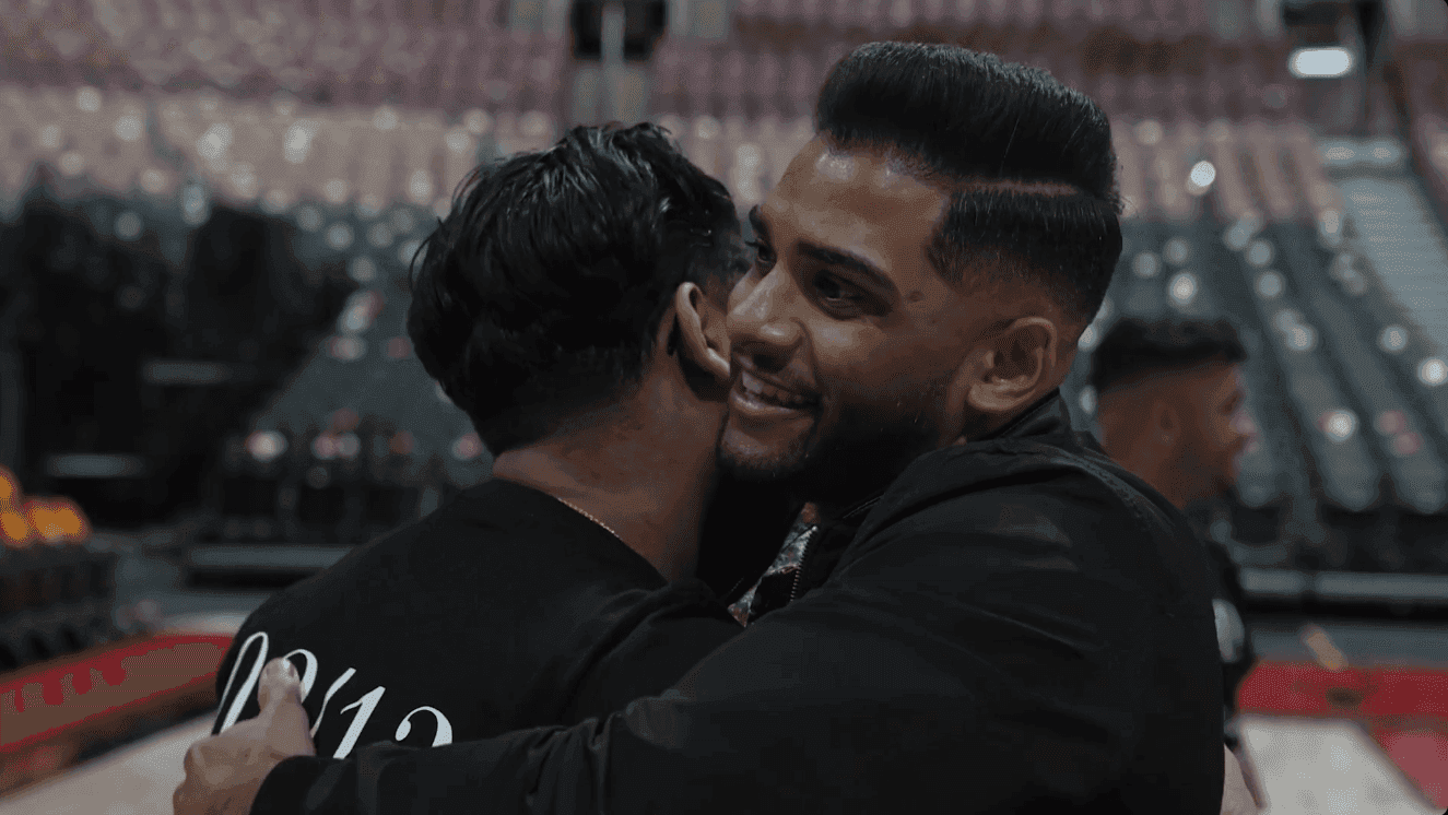Close-up of two male friends hugging after a surprise proposal in an empty Toronto Raptors arena, capturing a heartfelt and celebratory moment.