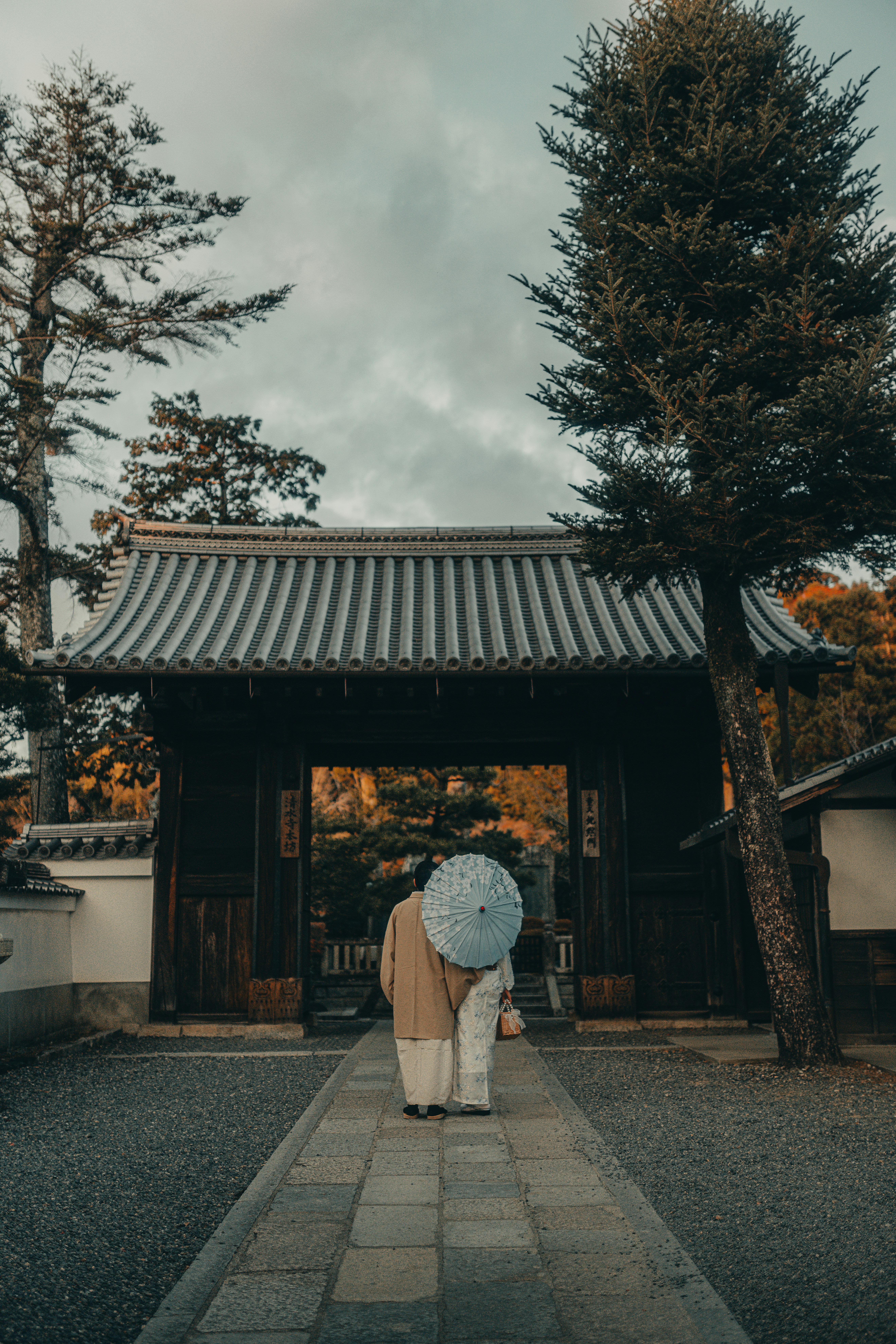 Two people with umbrella walk towards temple gate