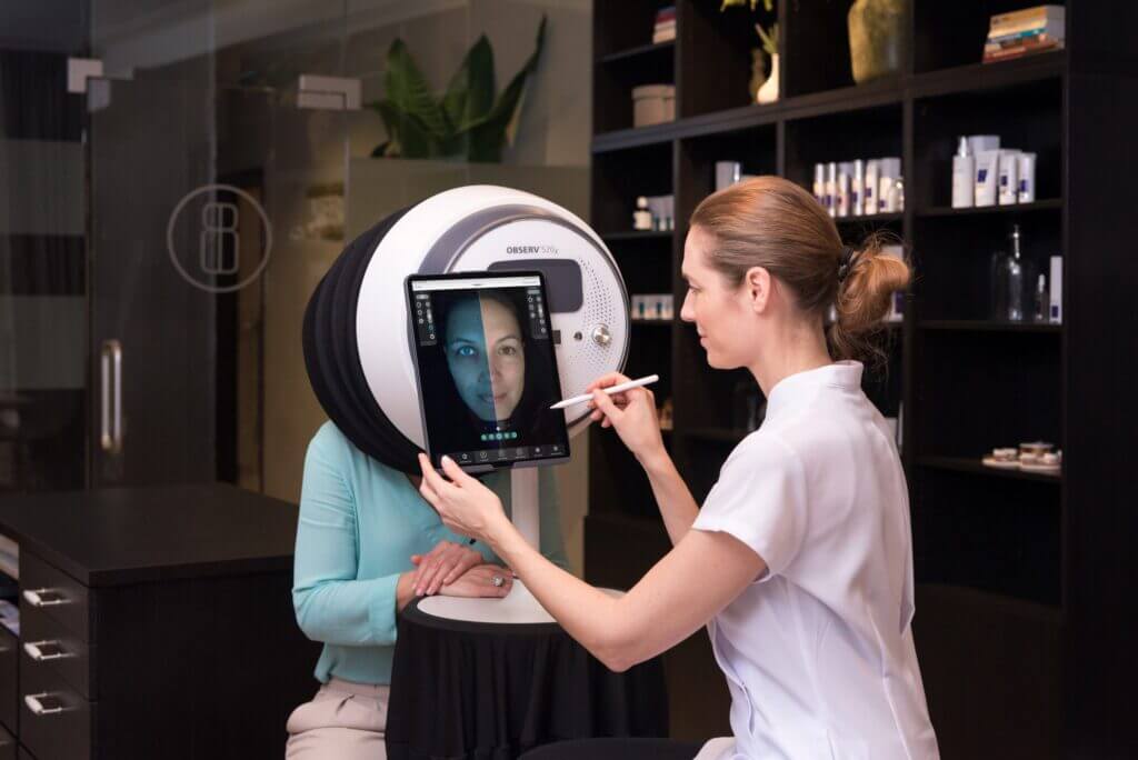 Specjalistka analizująca stan skóry twarzy klientki za pomocą profesjonalnego urządzenia.