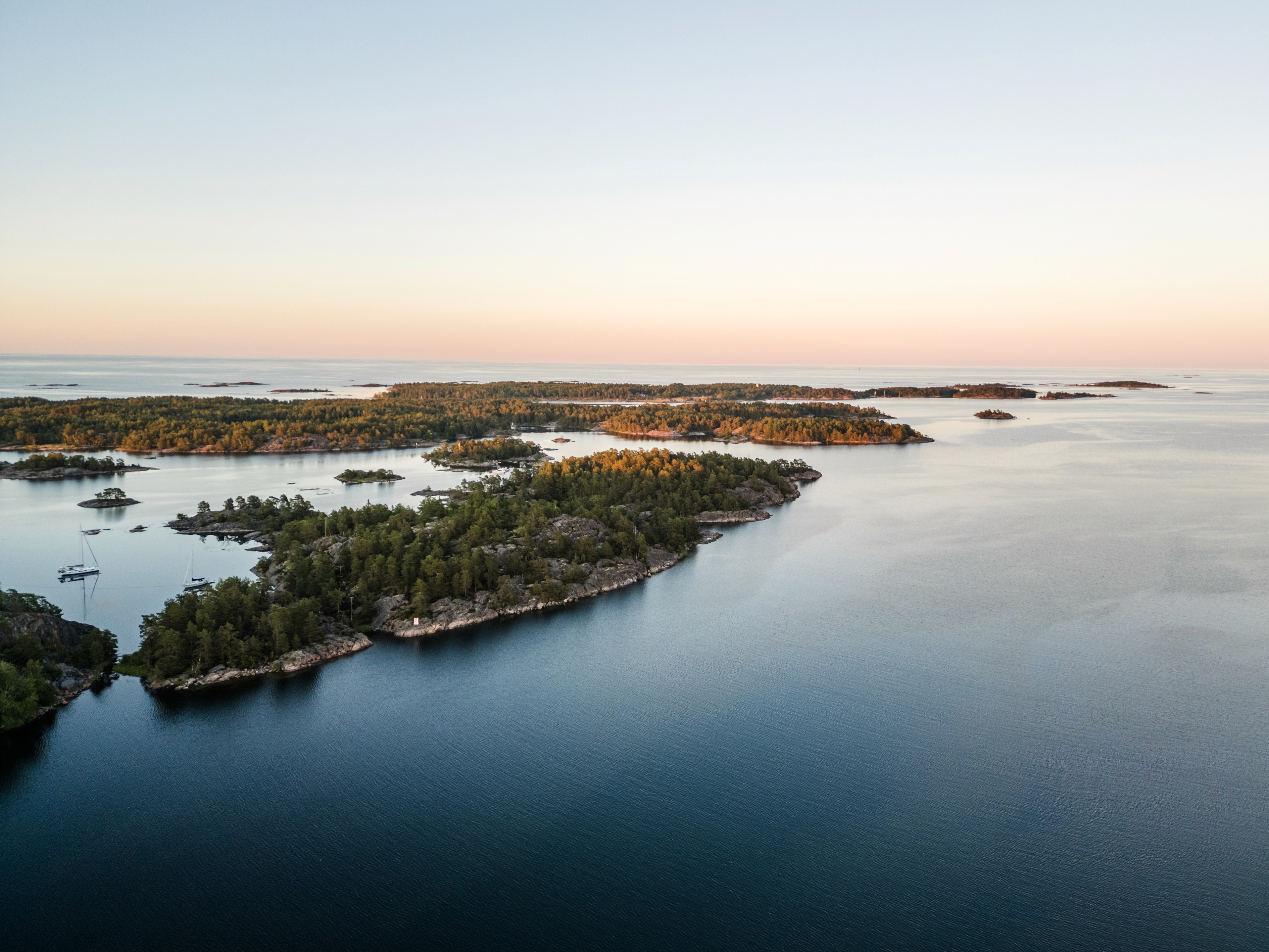 Landschaftsaufnahme von Schweden, im Hintergrund ist ein leichter Sonnenuntergang zu sehen, im Vordergrund sieht man die grüne Landschaft von Schweden
