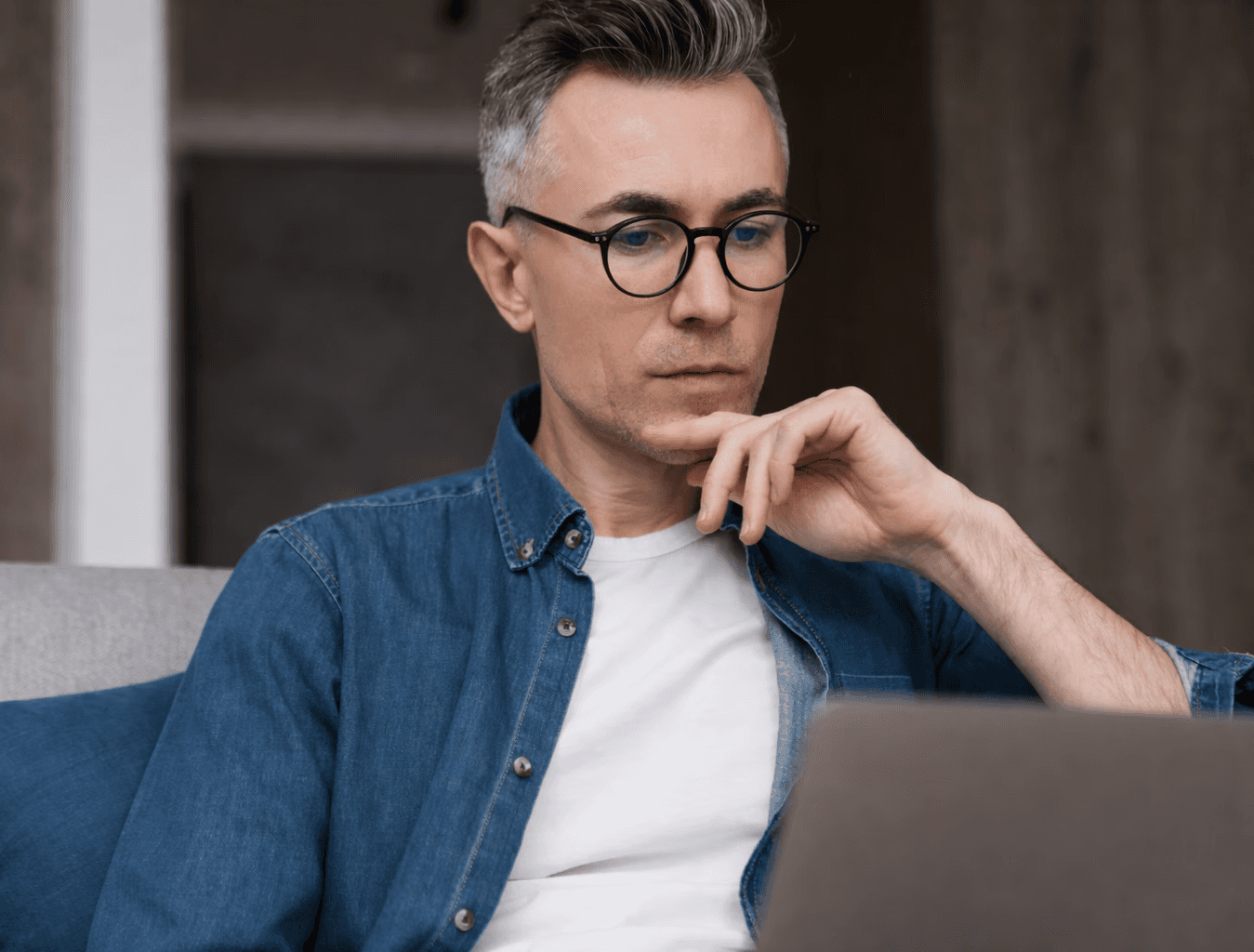 man sitting on couch with looking at his MacBook on table