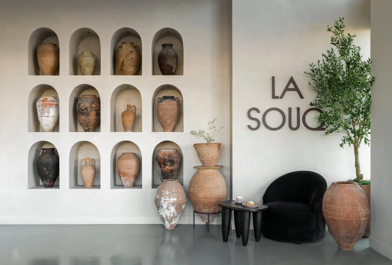 Interior of La Souq café in Dallas featuring arched wall niches with handcrafted pottery, warm neutral finishes, and minimalist La Souq signage creating a calm, design-led café space.