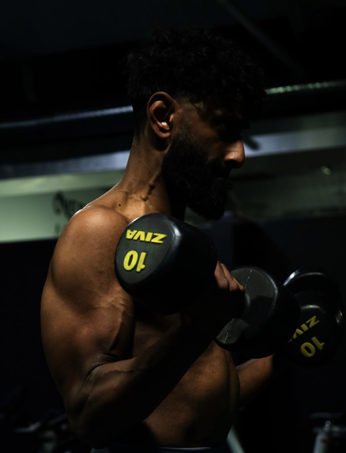 Male athlete performing a bicep curl with 10kg dumbbells in a dark fitness studio.