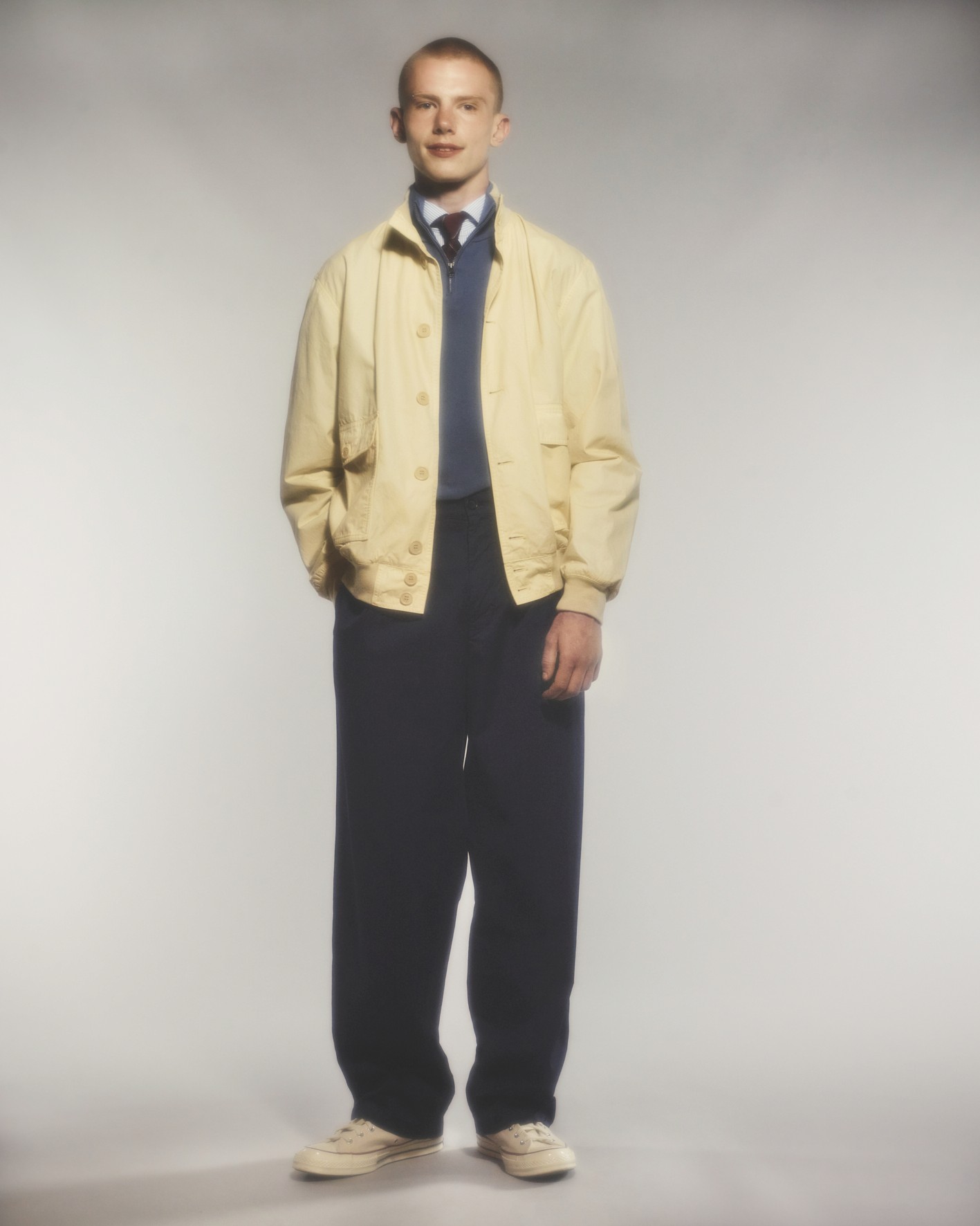 Sur fond neutre, le mannequin porte un blouson beige, un pantalon et un pull bleu dans le lookbook Aspesi 