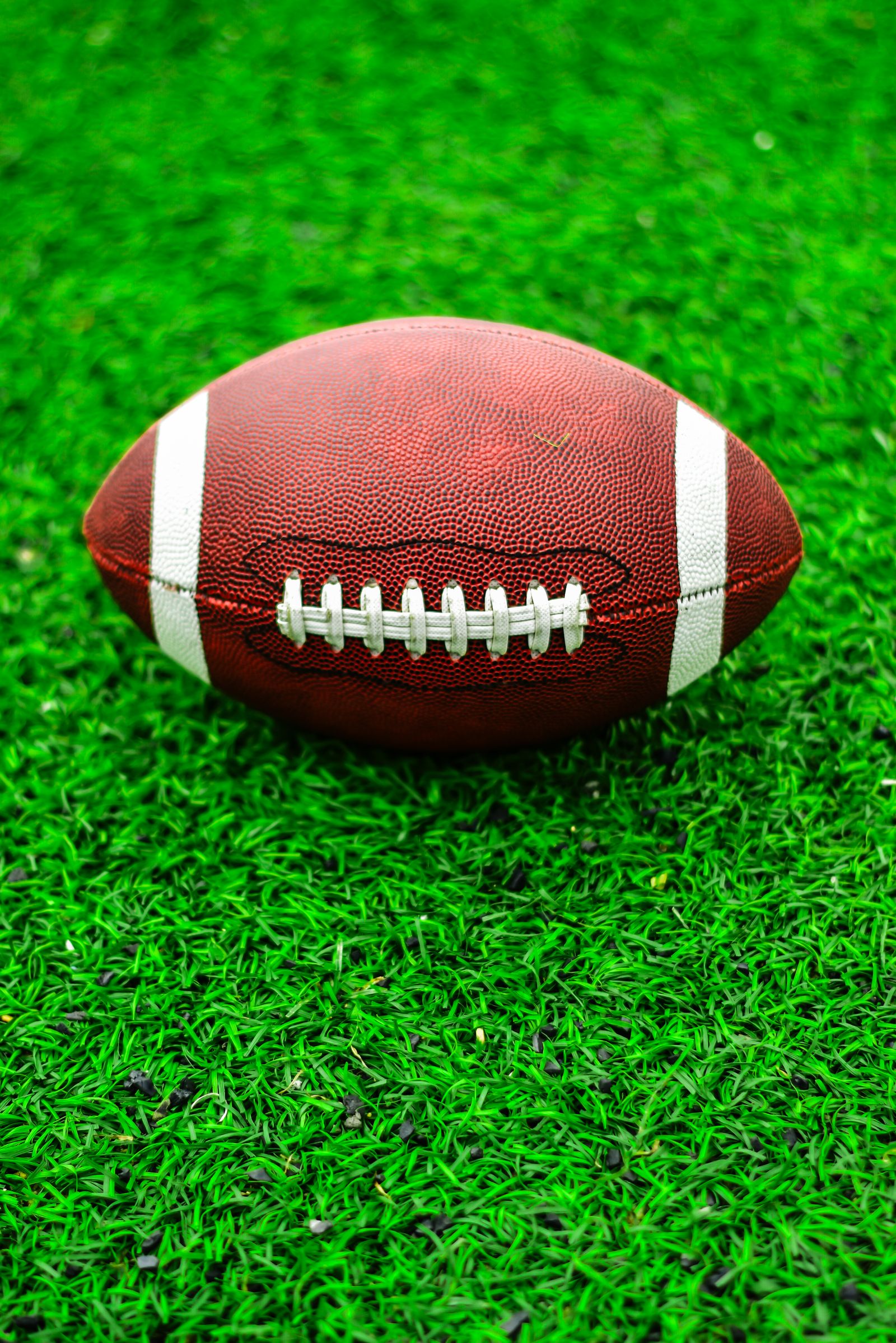 A brown American football resting on bright green turf in daylight