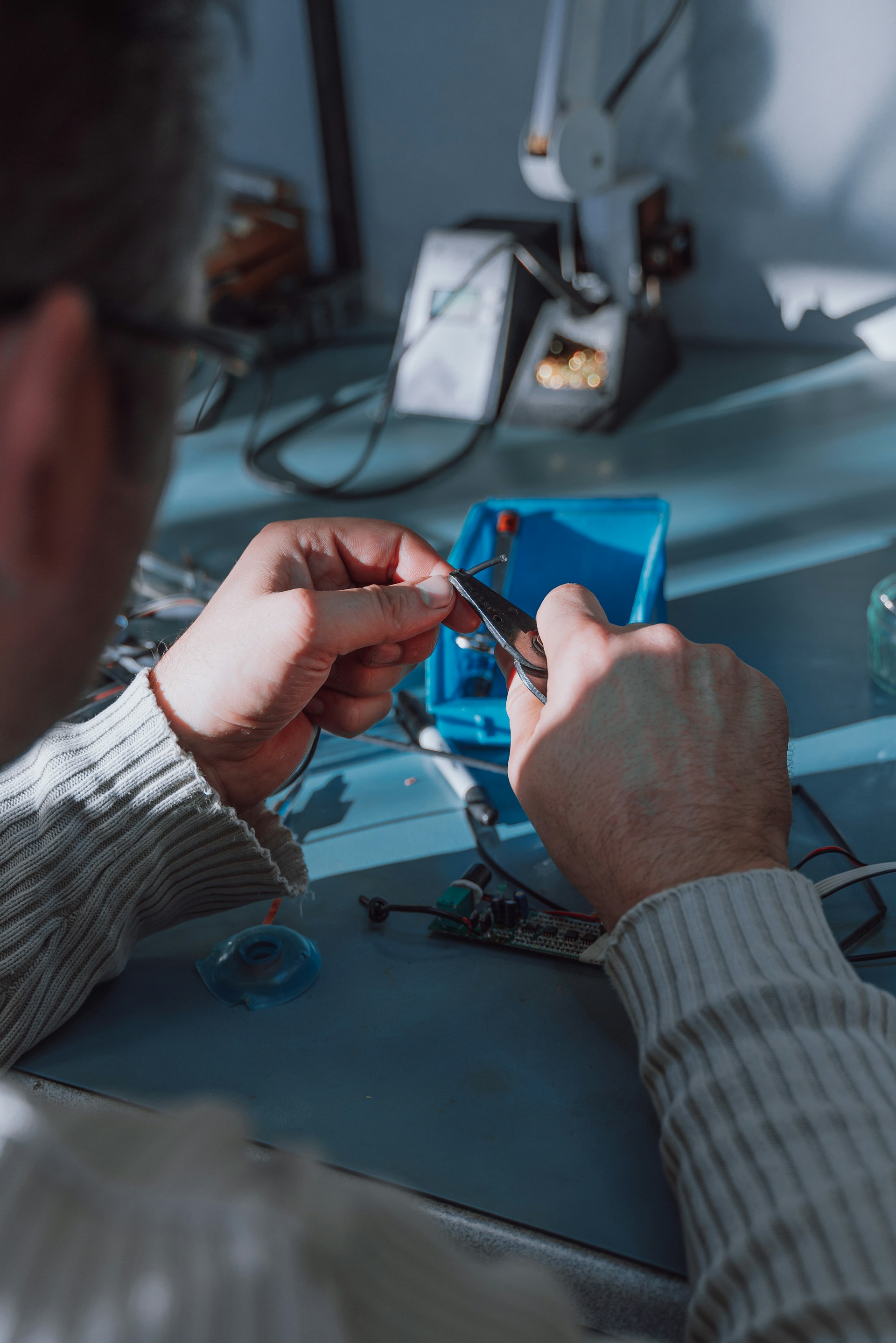 Technician stripping a wire with pliers over a workbench with a circuit board.