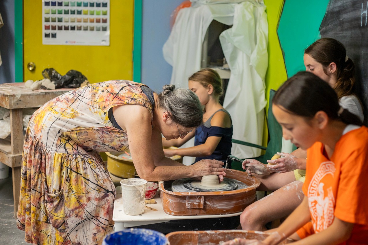 Instructor helping campers shape clay at the pottery wheel