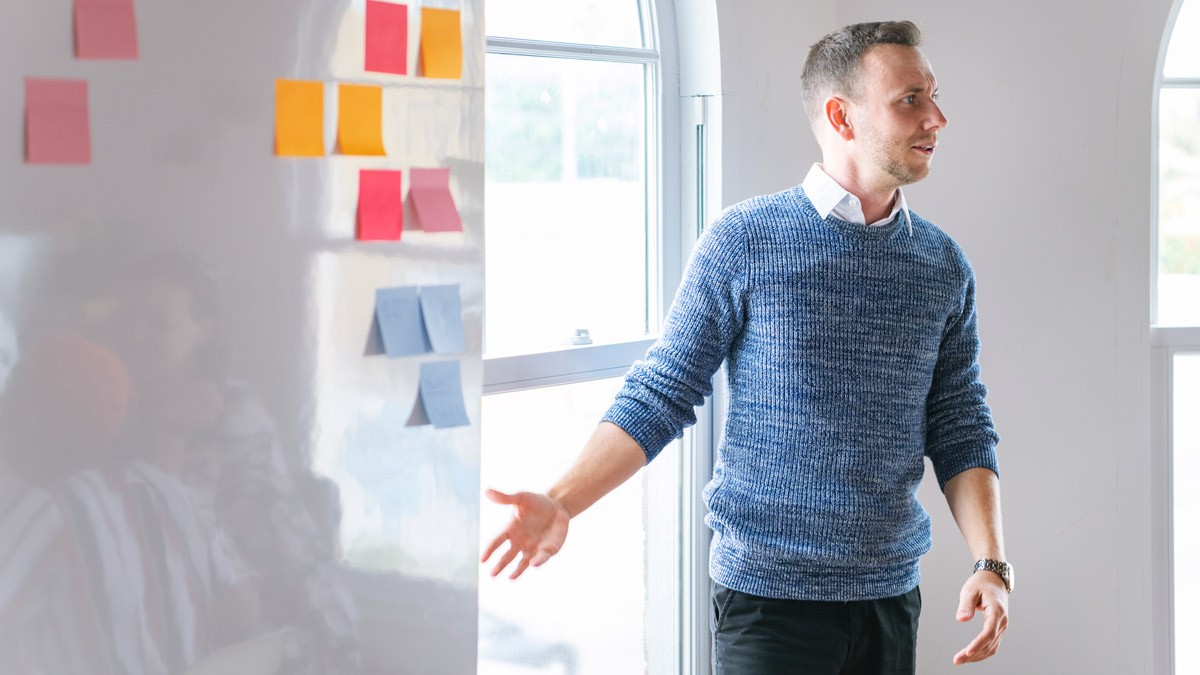 A workshop facilitator standing a front of a whiteboard filled with sticky notes and explaining workshop exercise. 