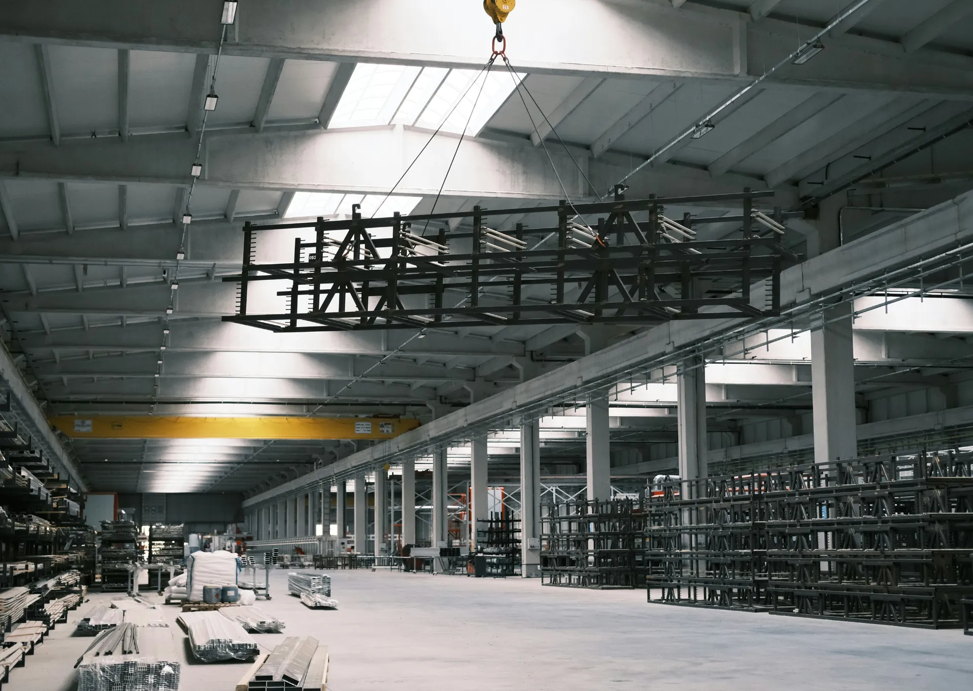 Structural steel truss lifting inside industrial fabrication facility with overhead crane and assembled steel members