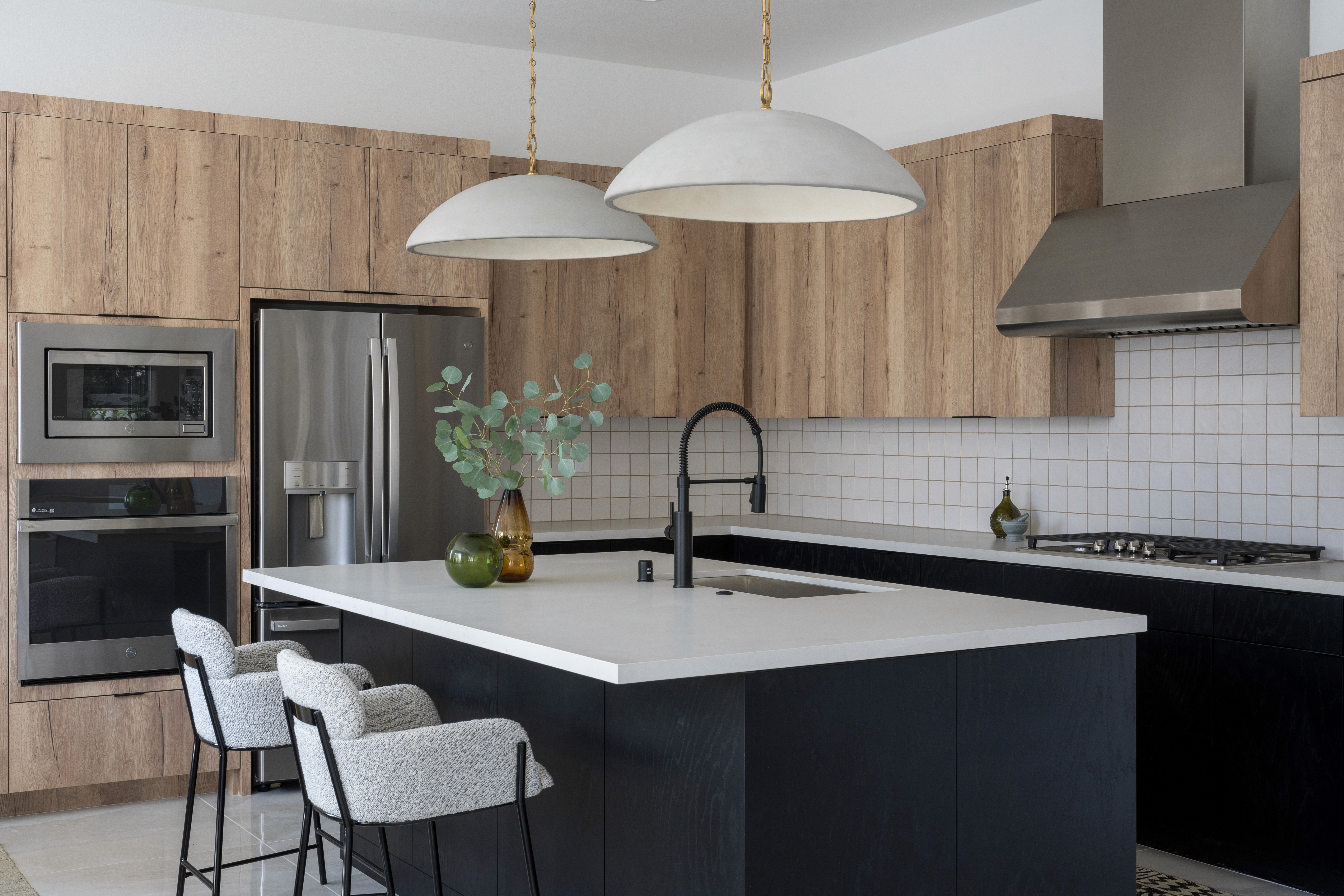 Moody kitchen with dark wood paneled island, white countertops, cool wood cabinetry, and large pendant lighting by Jubilee Interiors in Arcadia, California