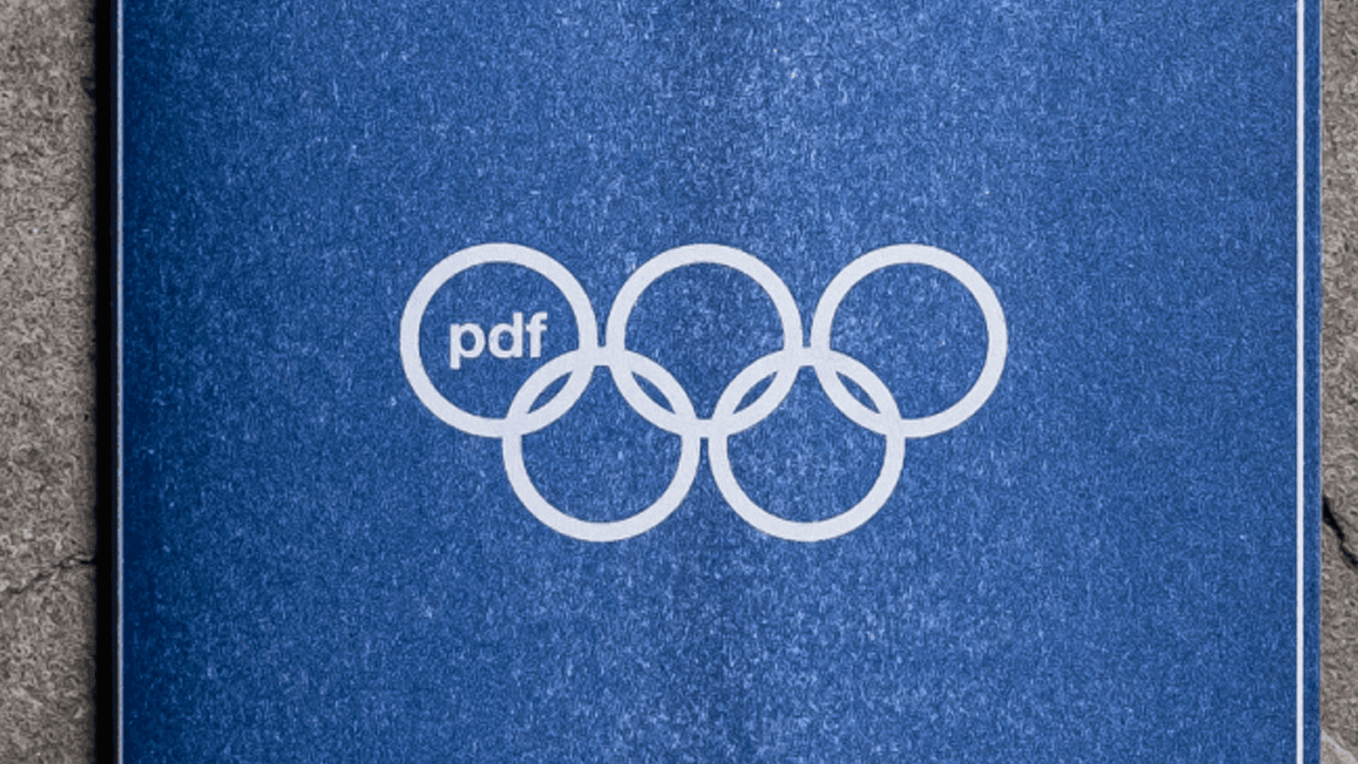 Archive PDF brand identity mockup featuring the pdf logo integrated into an Olympic style five ring symbol printed on a blue textured cover