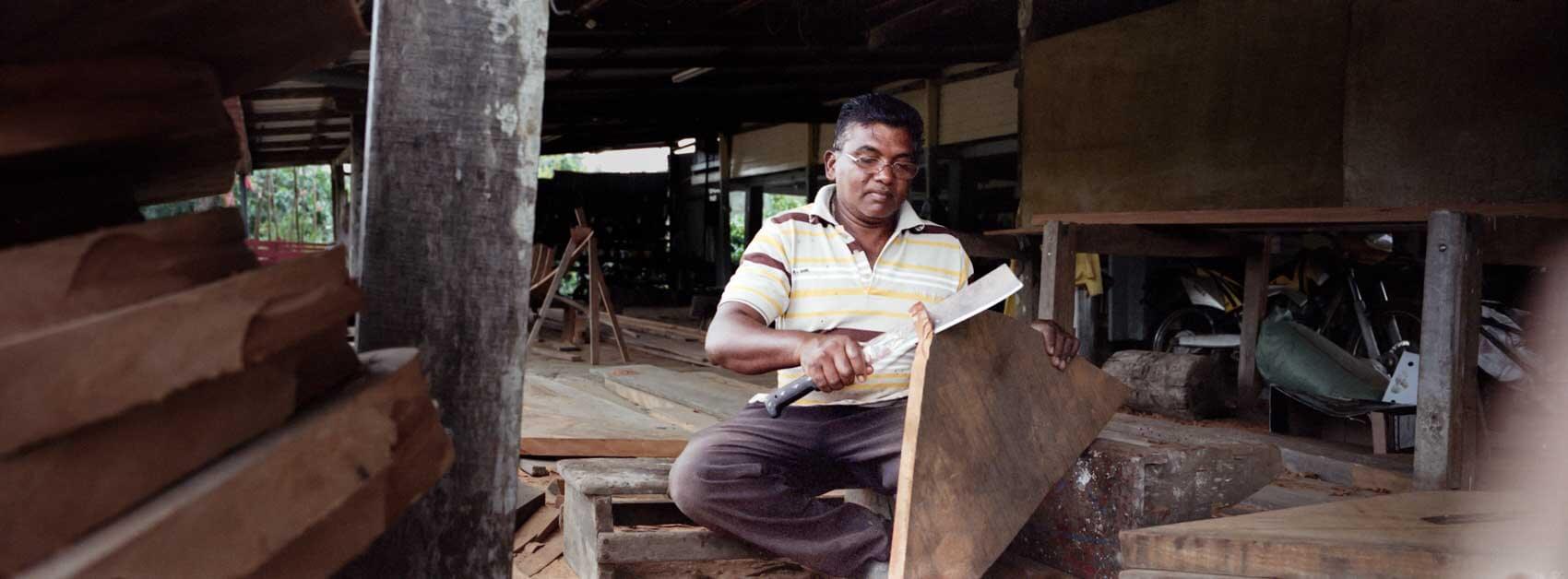 Traditional wooden boat builder in Suriname working inside a workshop, framed by wood, soft directional light shaping the scene, photographed on a Hasselblad Xpan and Kodak Portra. 