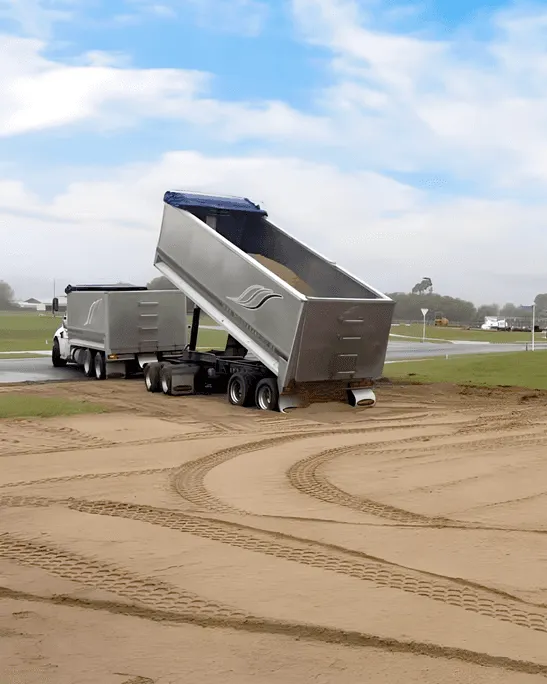 Large semi-truck trailer unloading sand onto a building site foundation