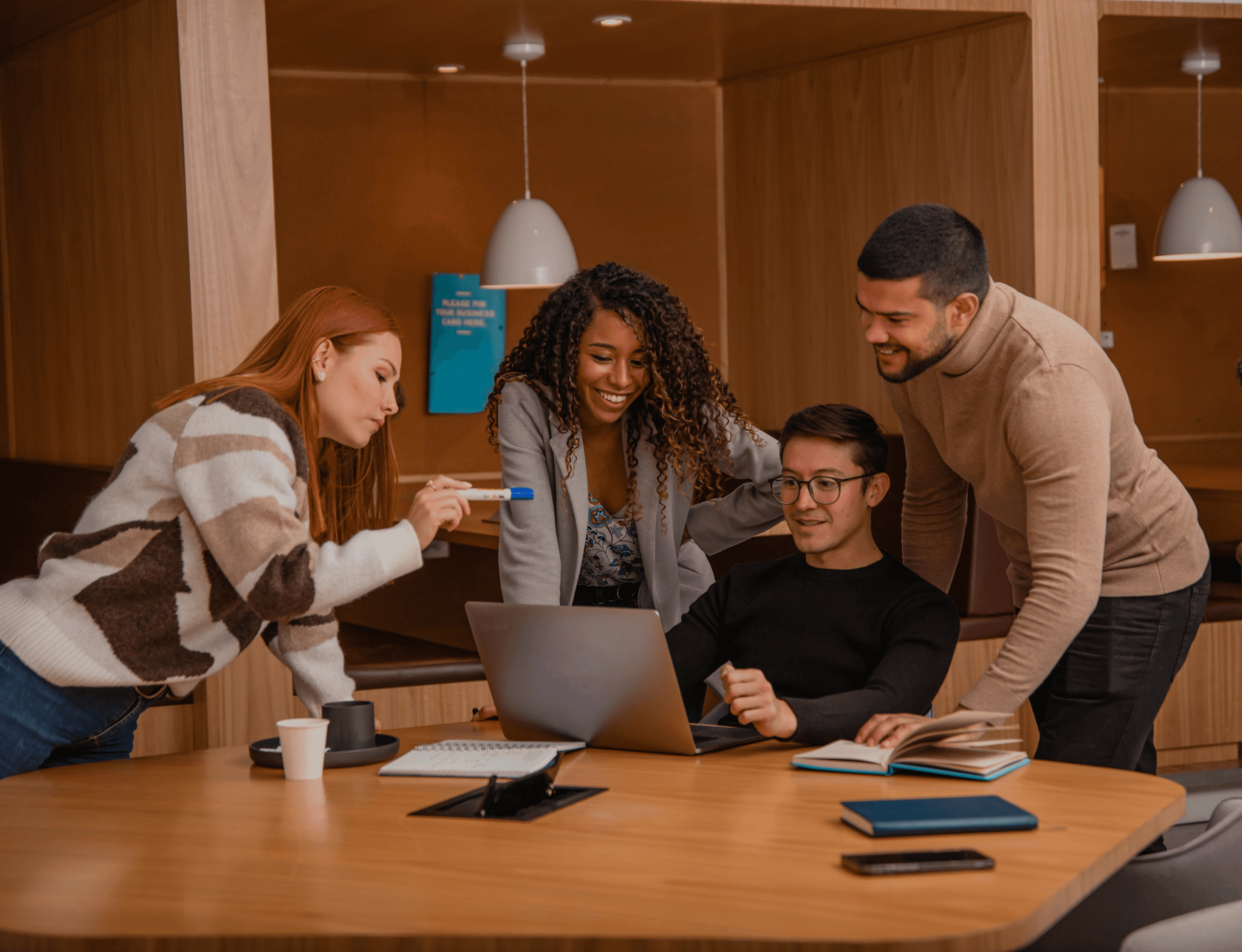 Four people collaborating around laptop in workspace