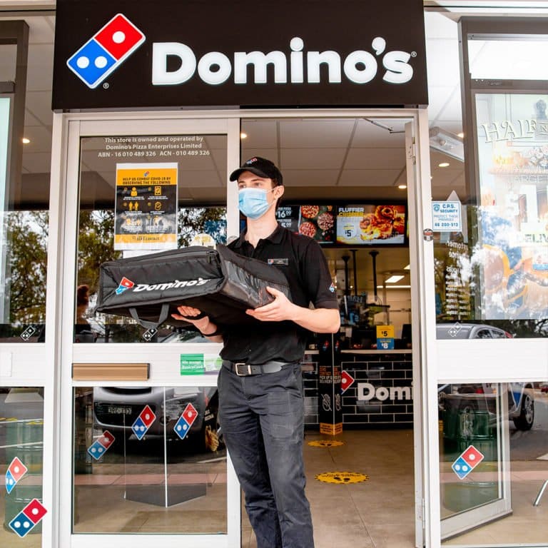 Domino's employee carrying a pizza delivery bag out of a Domino's store
