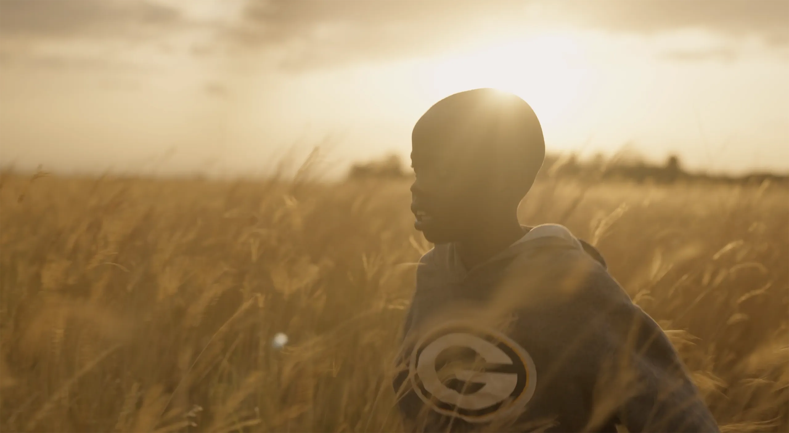 A beautiful wide shot of a child standing in a golden wheat field during sunset with soft cinematic light.