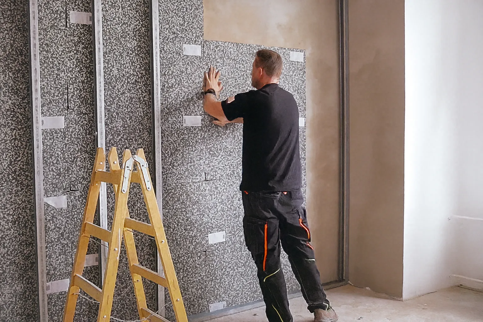 Osoba v rukavicích instaluje panel na stěnu a používá vodováhu pro přesné srovnání.