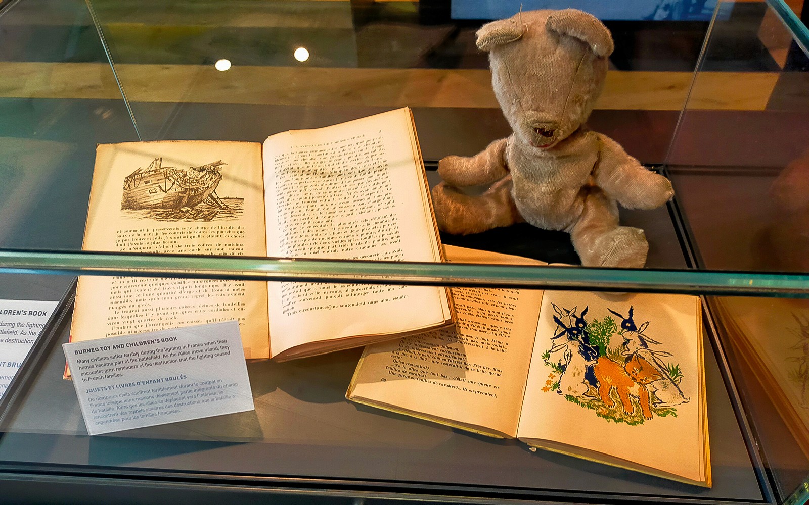 Burned toy and children's books displayed at D-Day Normandy museum exhibit.