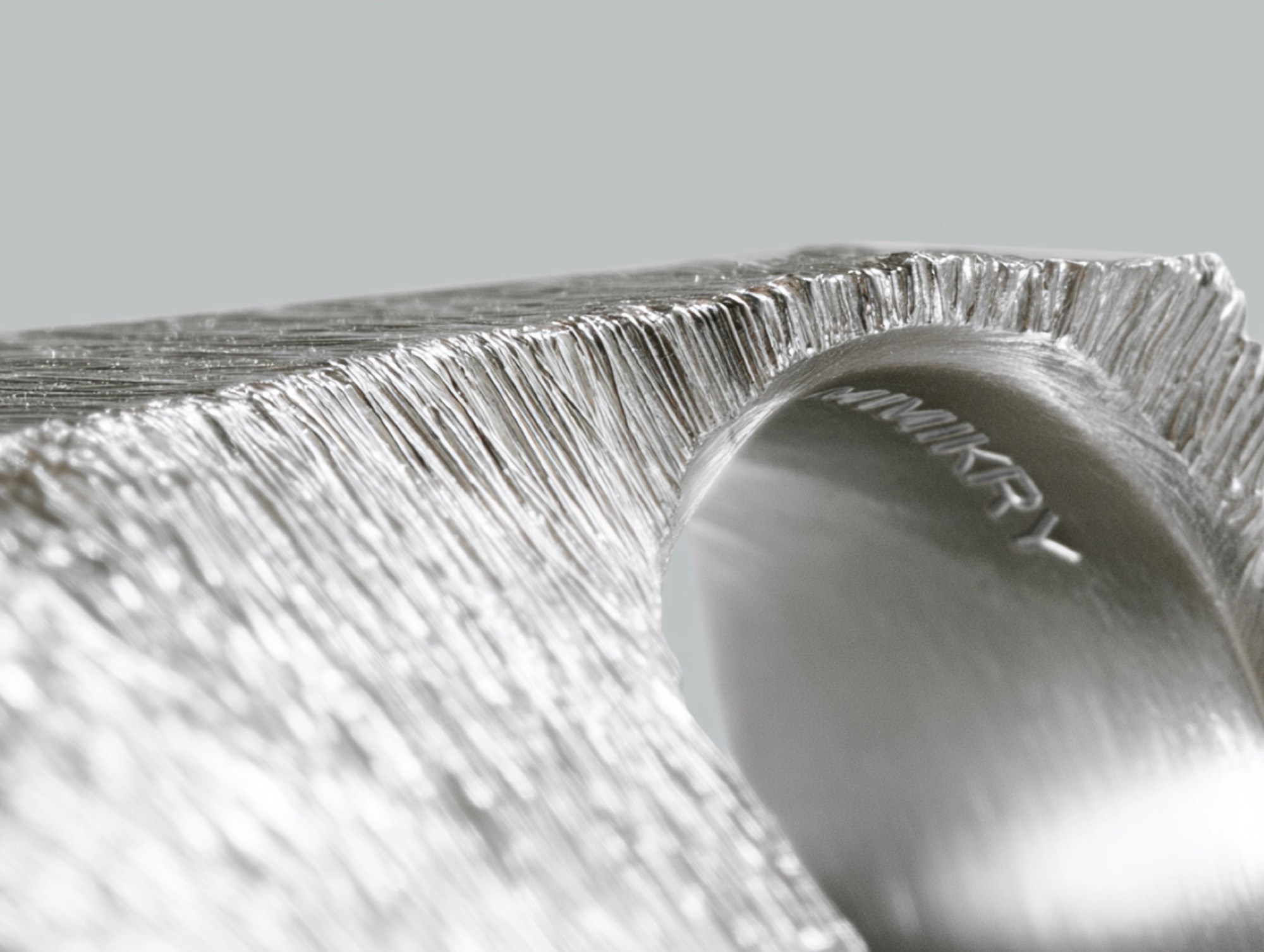 Brushed silver object with a polished curve engraved with the mimikry wordmark