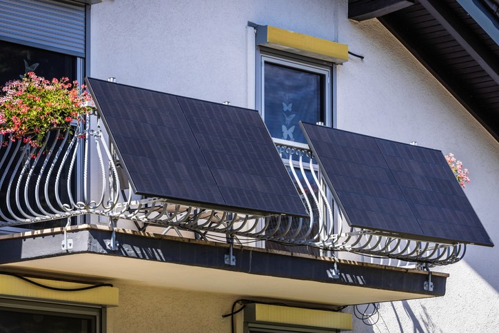 Zwei Solarpaneele an einem Balkongeländer, auf einem davon ein Blumentopf, im Hintergrund die blaue Außenfassade des Gebäudes.