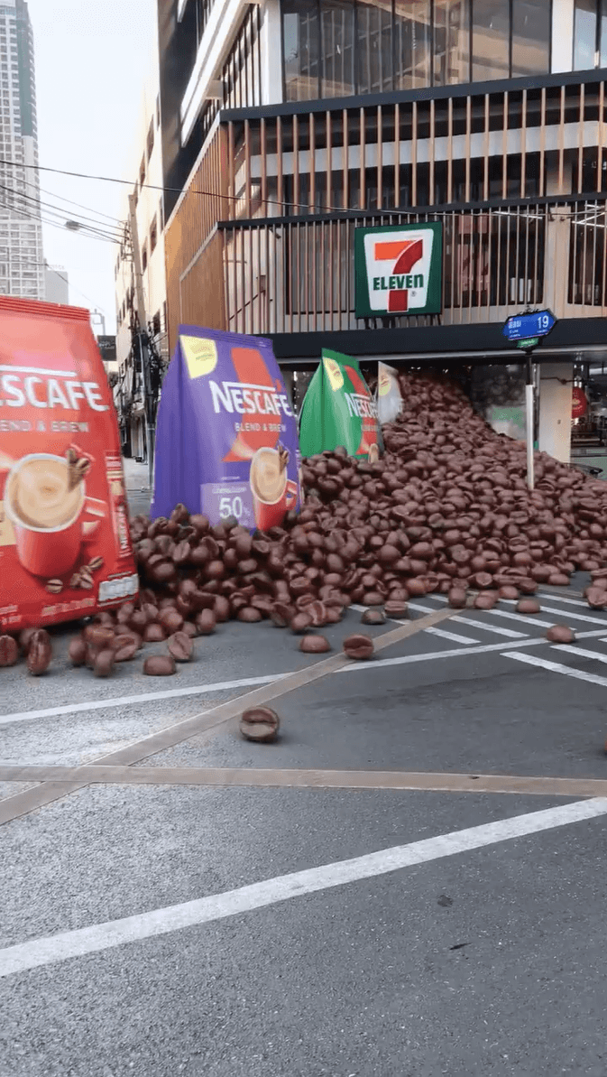 Massive bags of Nescafé coffee spilling giant beans across a city street in front of a 7-Eleven