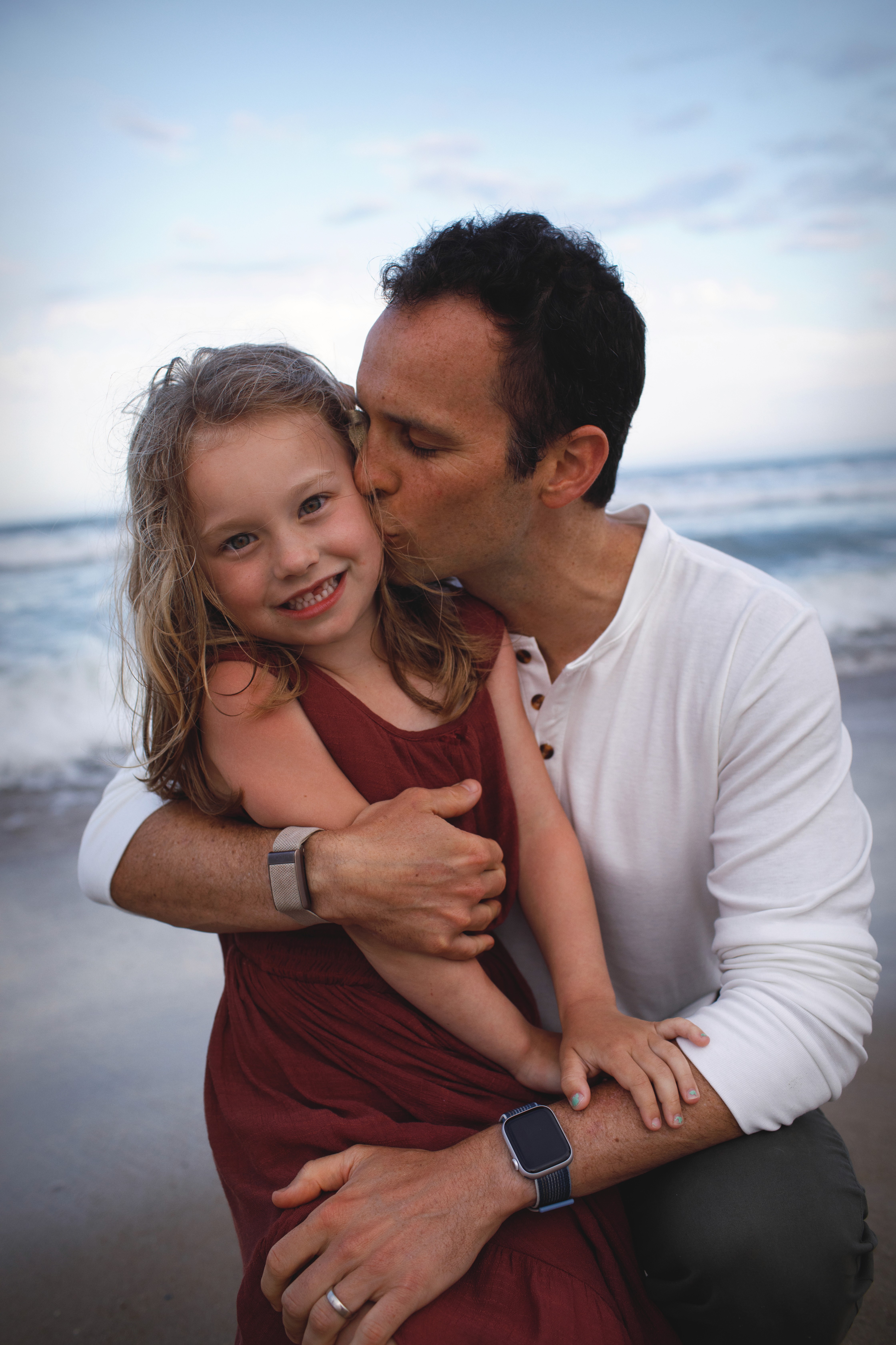 Dad hugging his laughing daughter during a warm sunset beach session.
