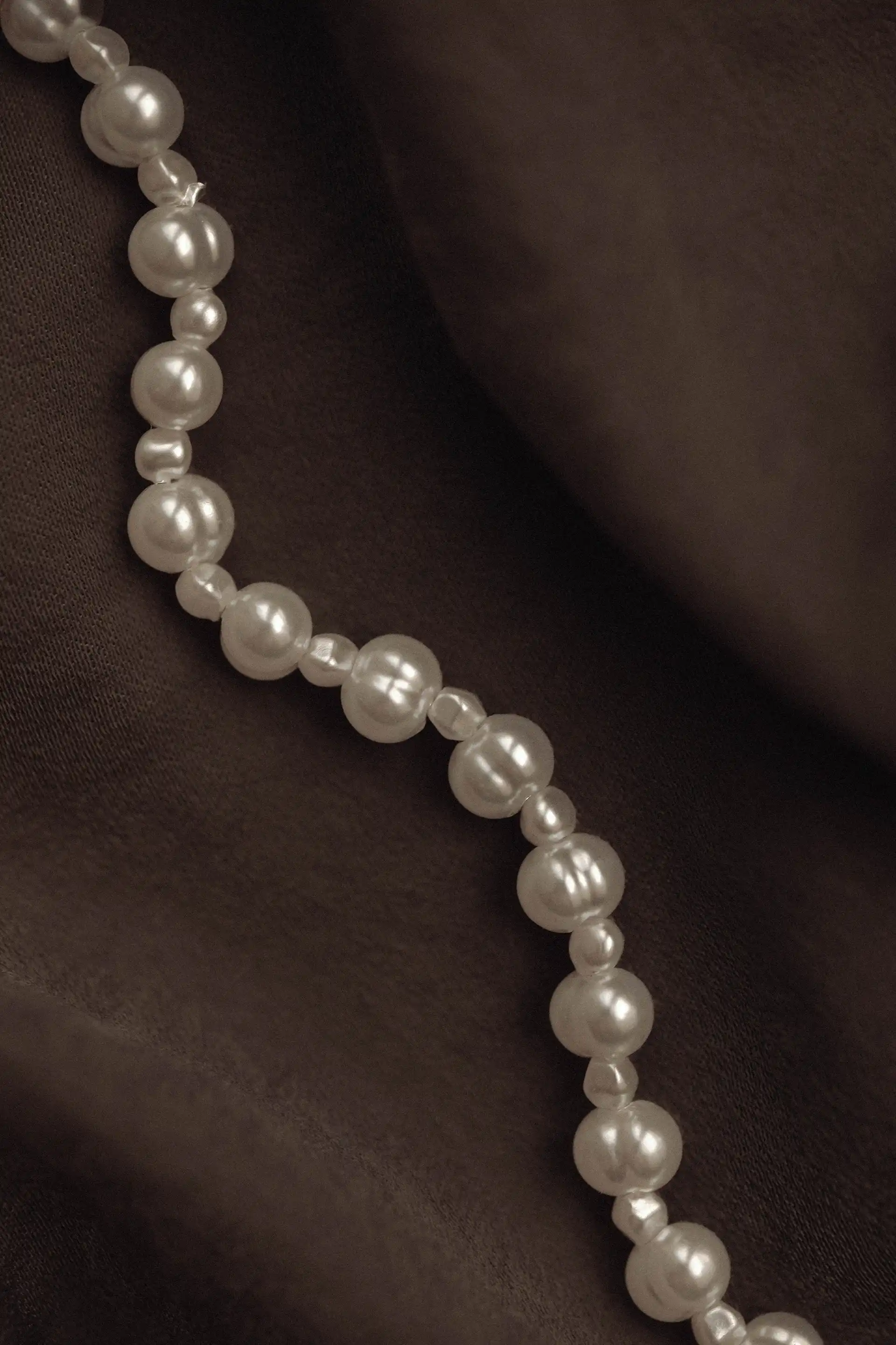 Perlenkette auf dunklem Stoff mit weichen Falten, sanftes Licht und dezente Reflexionen