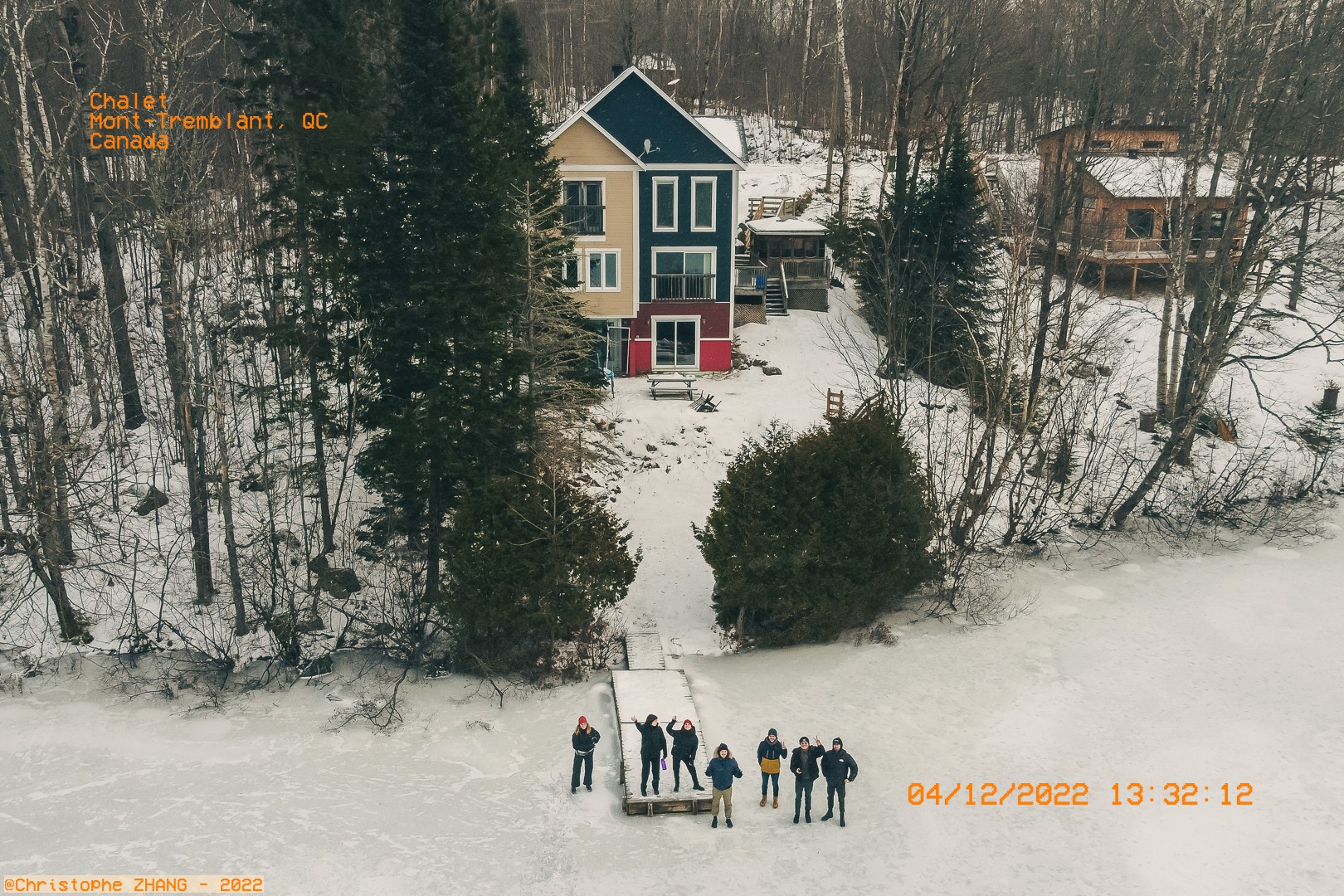 Groupe de personnes saluant depuis un quai enneigé devant un chalet.
