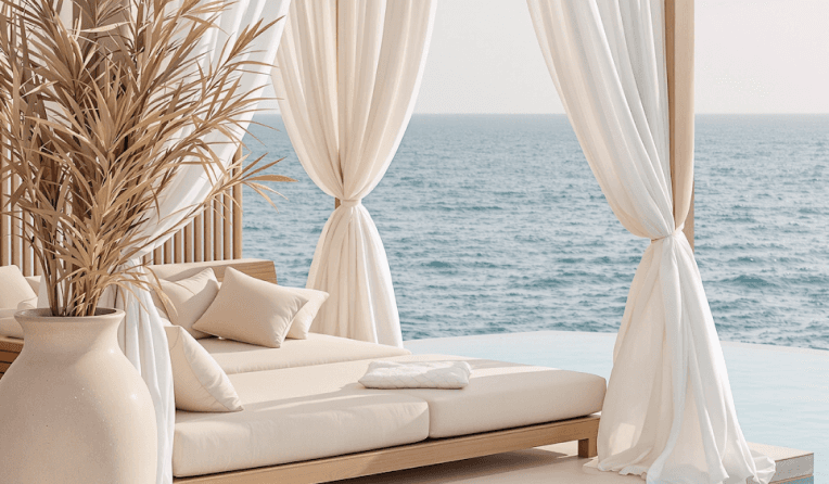 Luxury seaside lounge with white curtains, beige cushions, and ocean view.