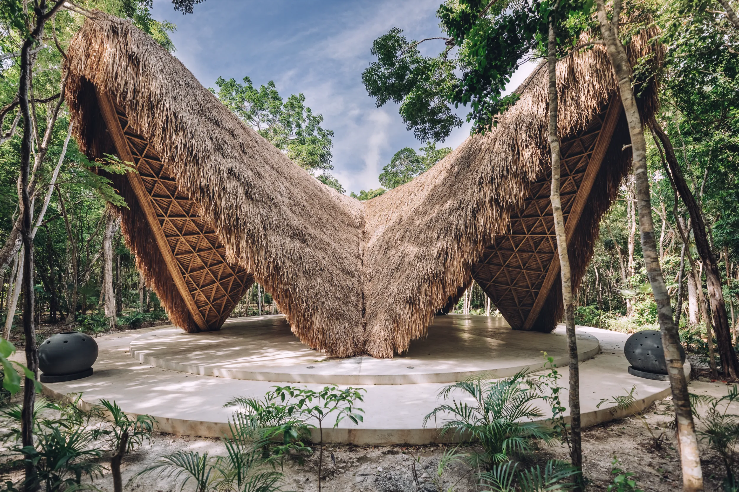Exterior view of the iconic Luum Temple bamboo pavilion in Tulum, featuring its signature five-sided catenary structure and thatched roof against the jungle backdrop.