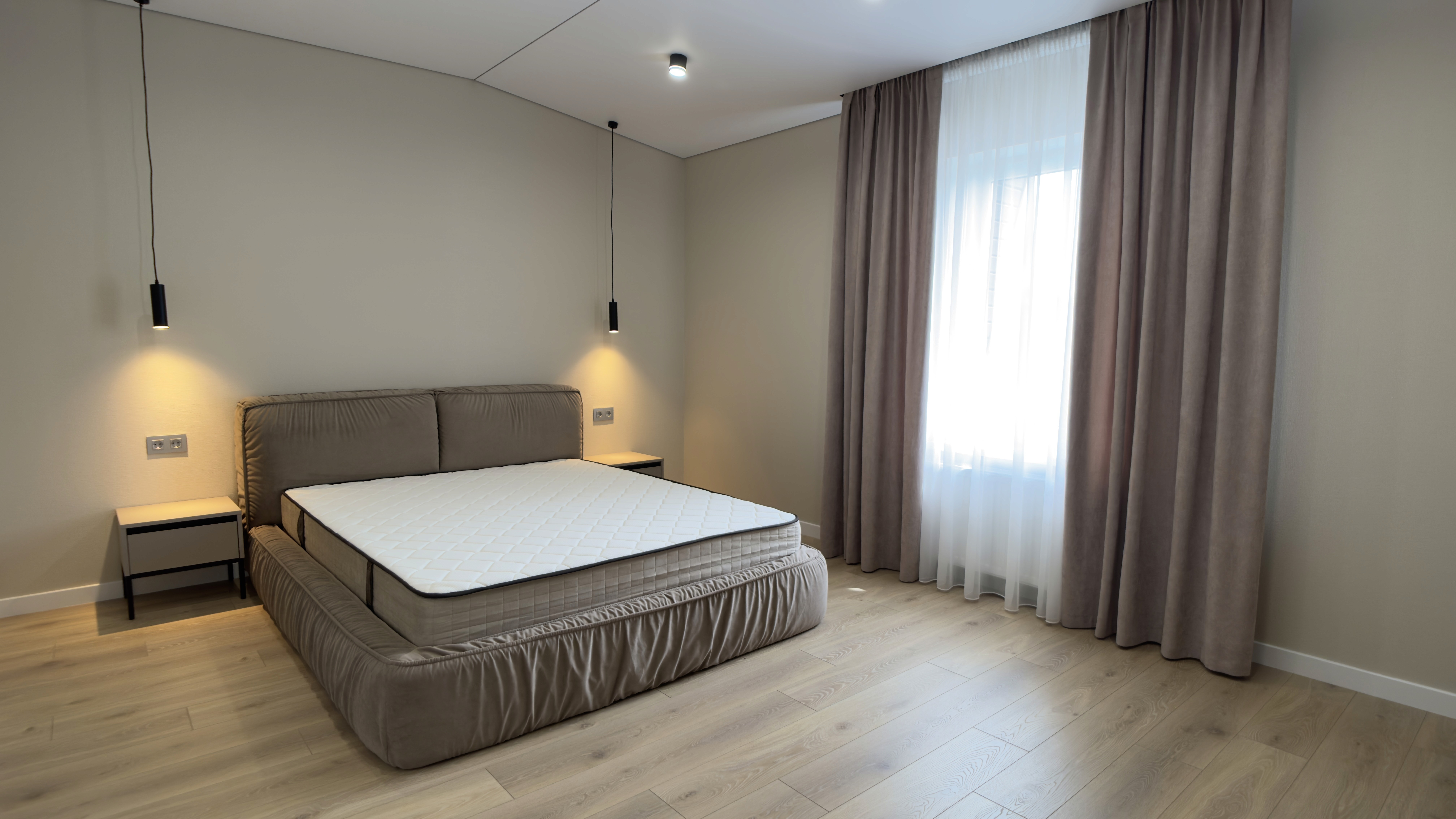 Мінімалістична спальня з великим ліжком, підвісними світильниками та дерев’яною підлогою