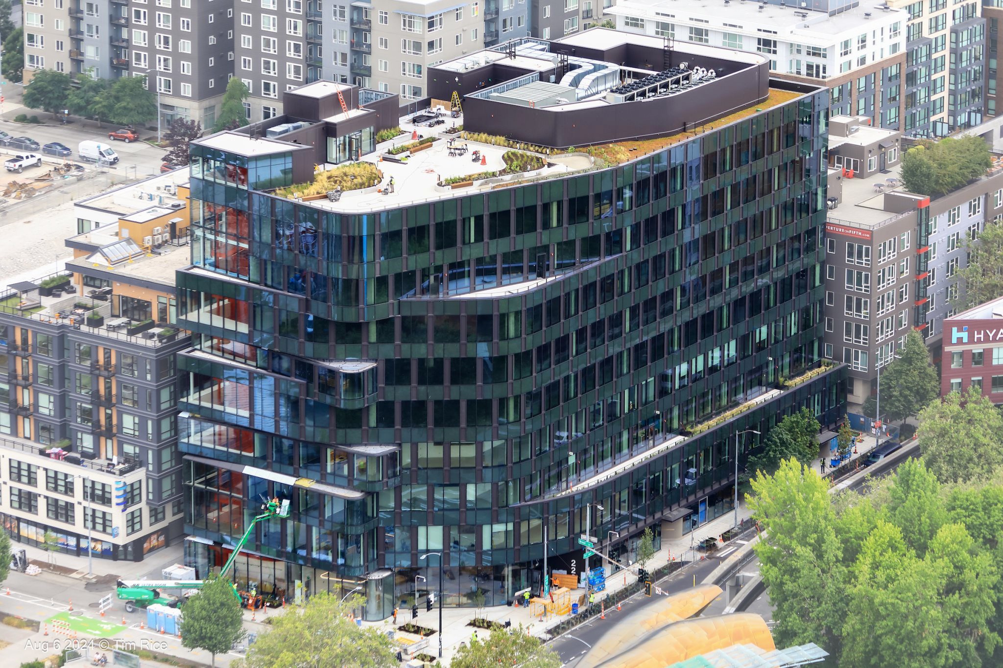 Aerial view of the building under construction, showcasing its undulating facade, vibrant amenity staircase, and lush green roof.