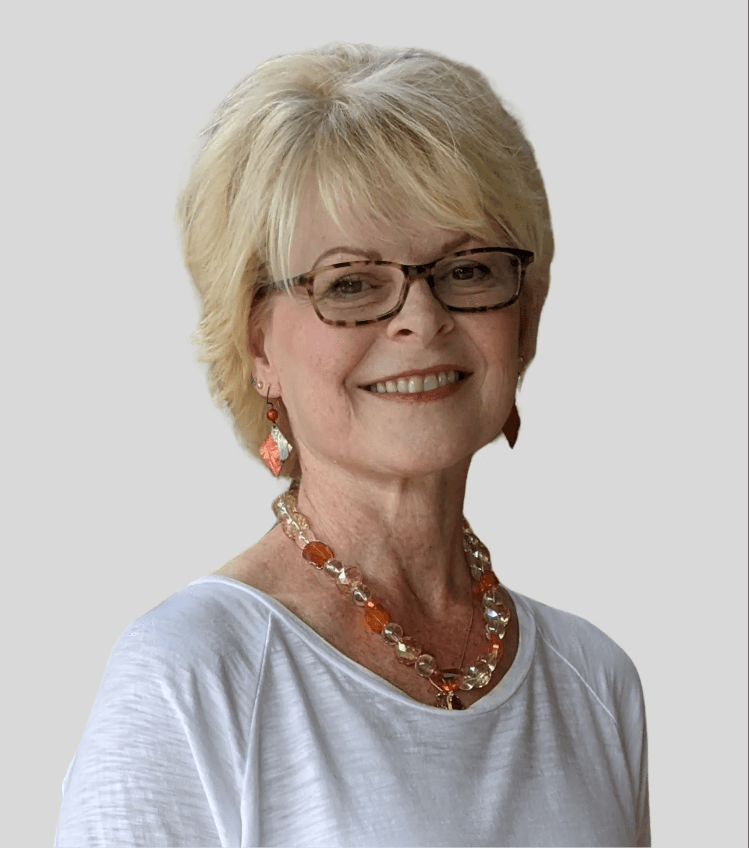 Smiling mature woman with short blonde hair and glasses wearing an orange beaded necklace.