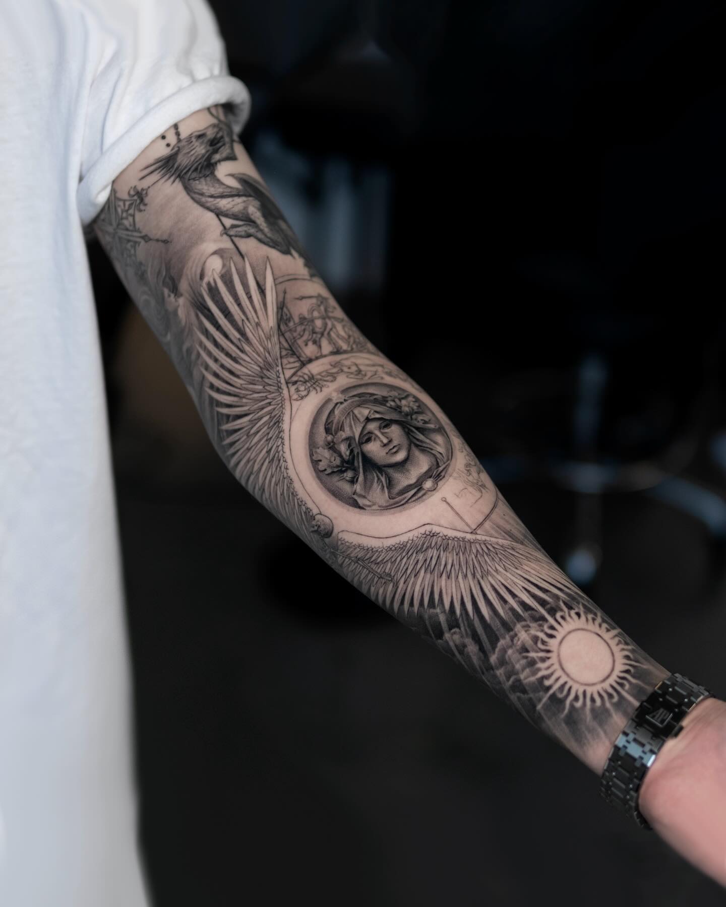 A detailed sleeve tattoo on a man's arm, featuring a woman's face surrounded by wings and celestial imagery.