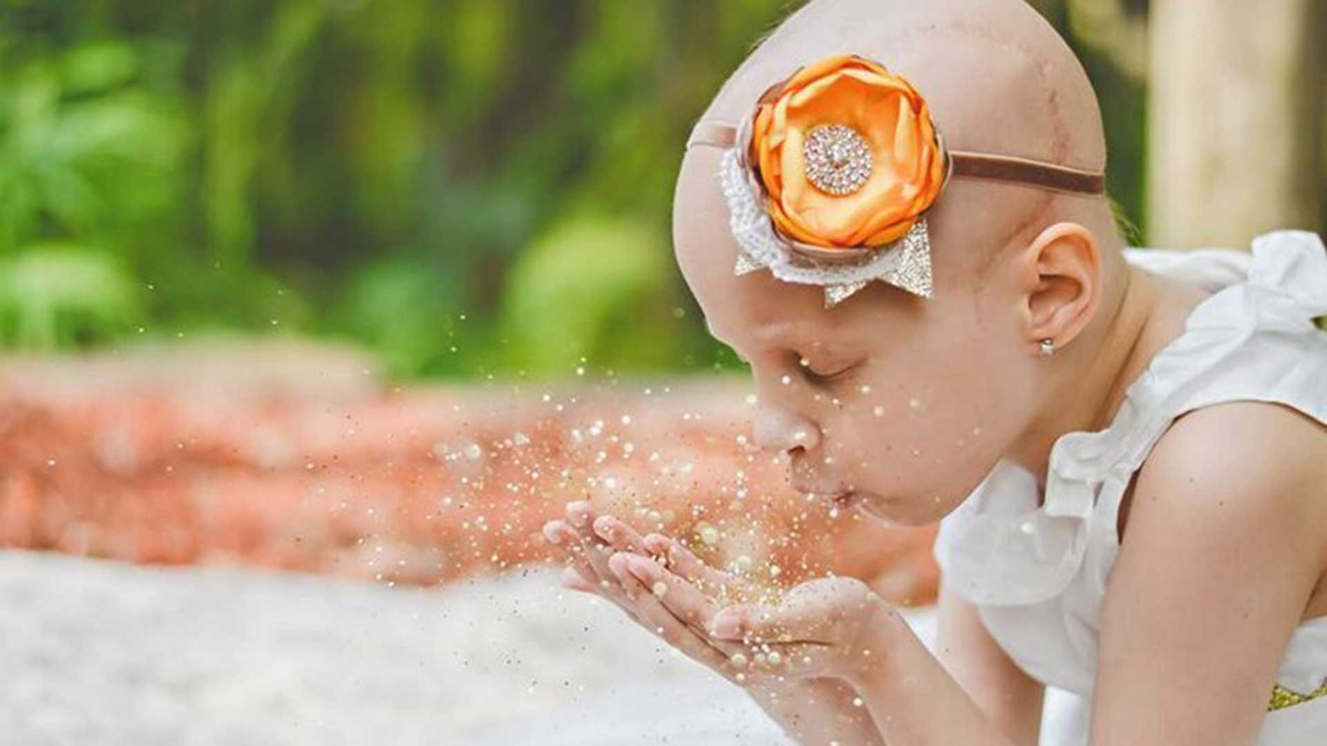 young girl cancer patient blowing glitter into the air