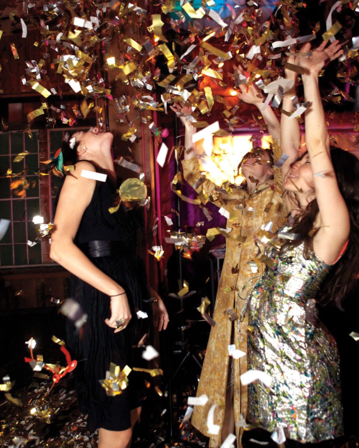 Guests dressed in glam NYE outfits holding cocktails at a dimly lit party.