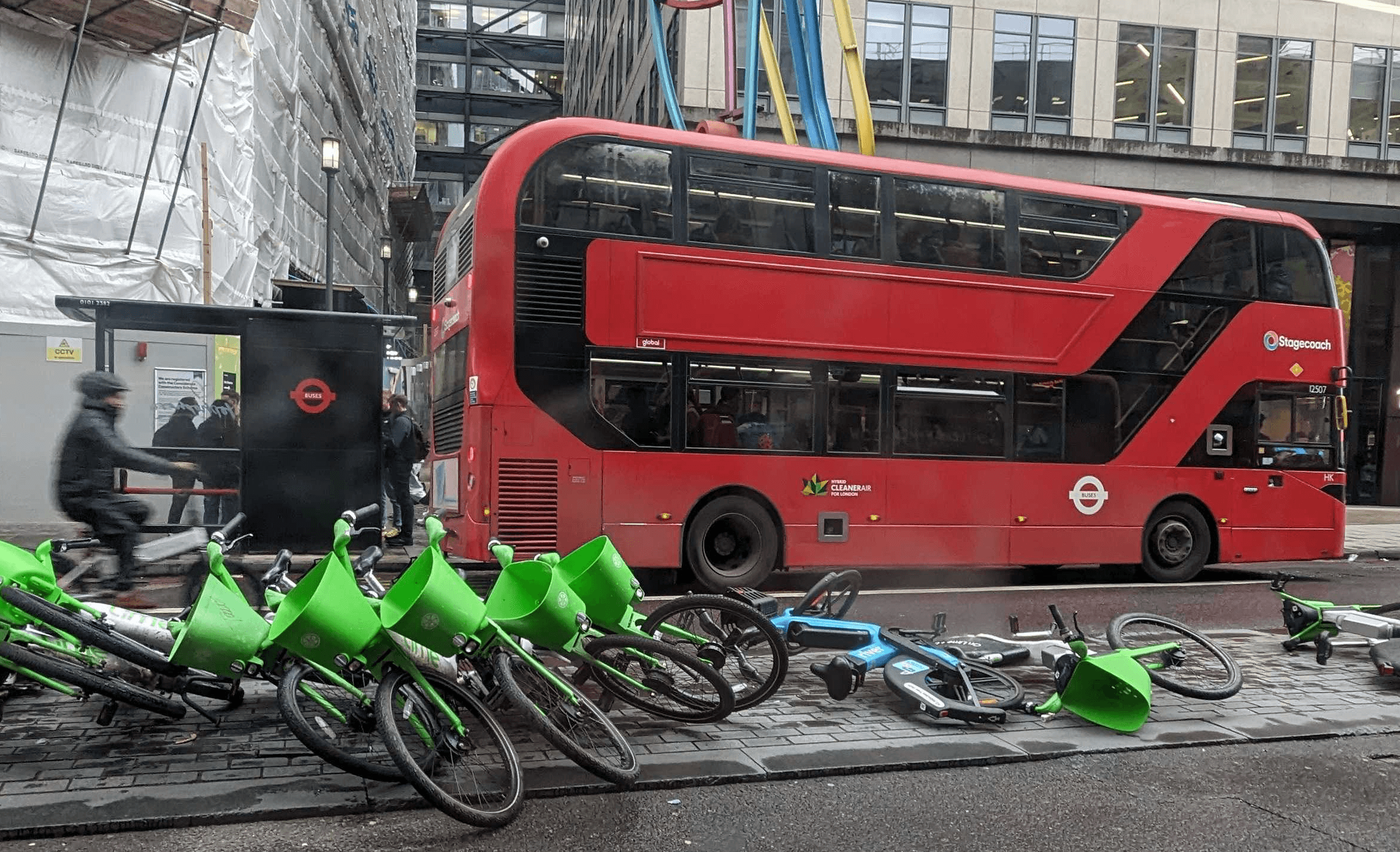 A row of e-bikes lying on their sides blocking a pavement with a London red bus behind it.