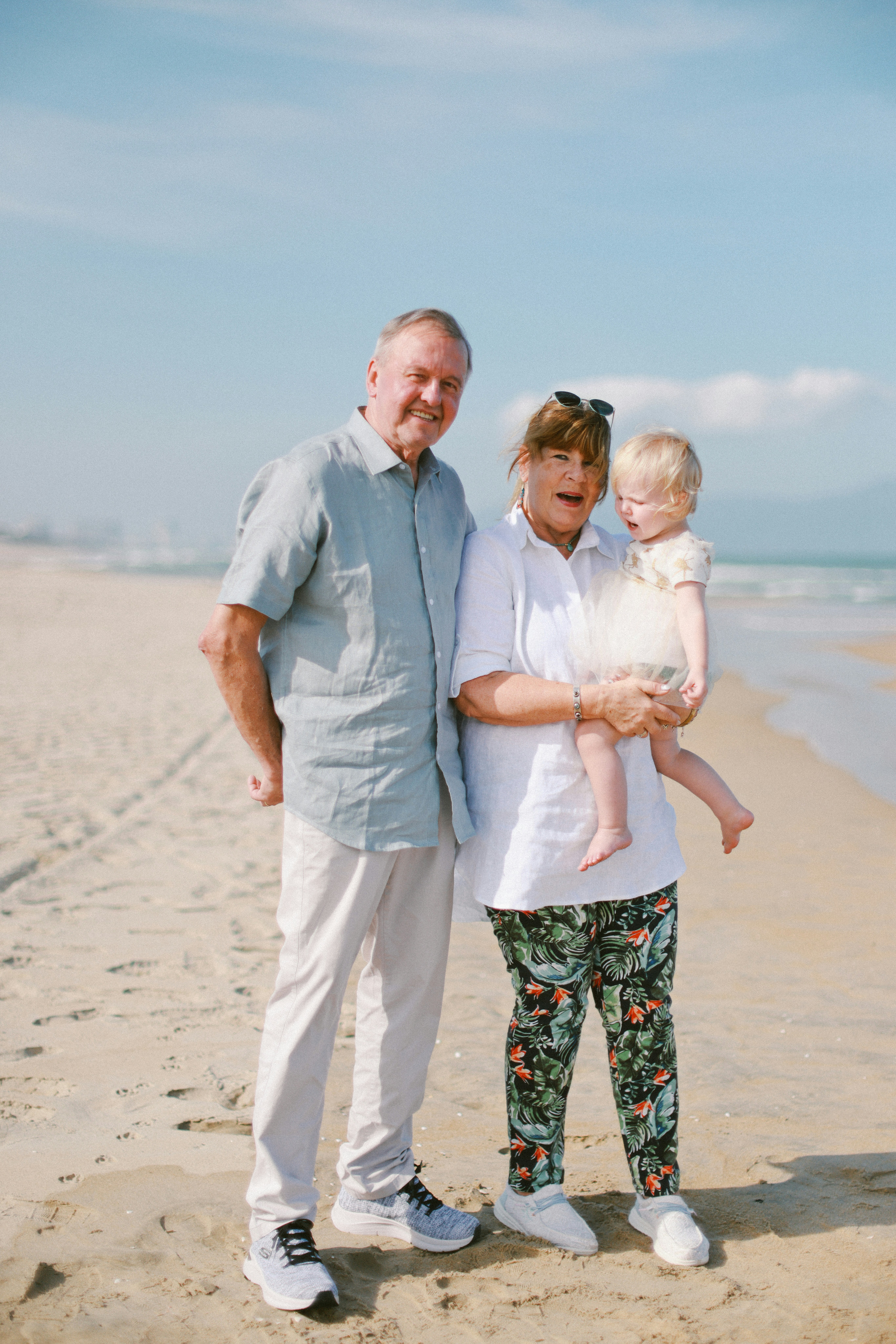 Grandparents holding a baby on a sunny beach